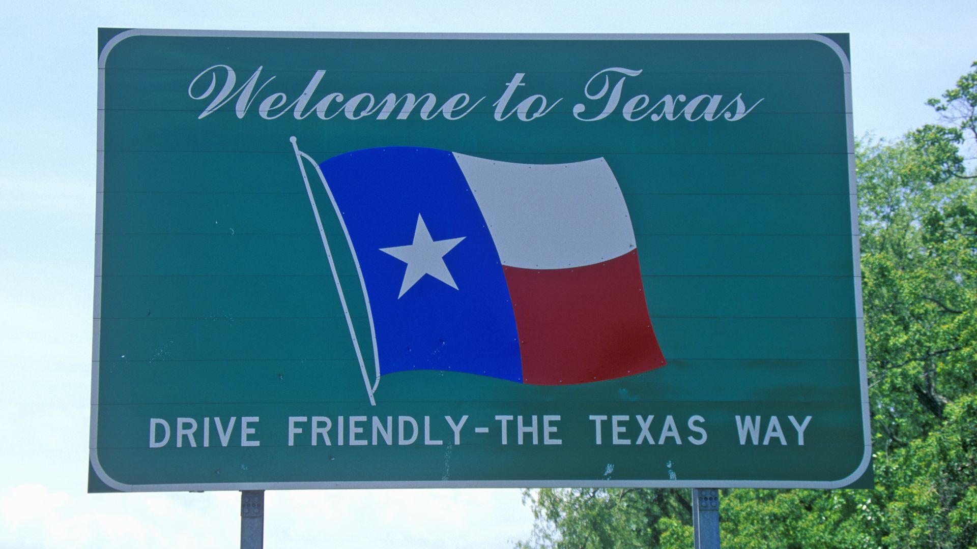 A green road sign that says Welcome to Texas above a Texas flag.