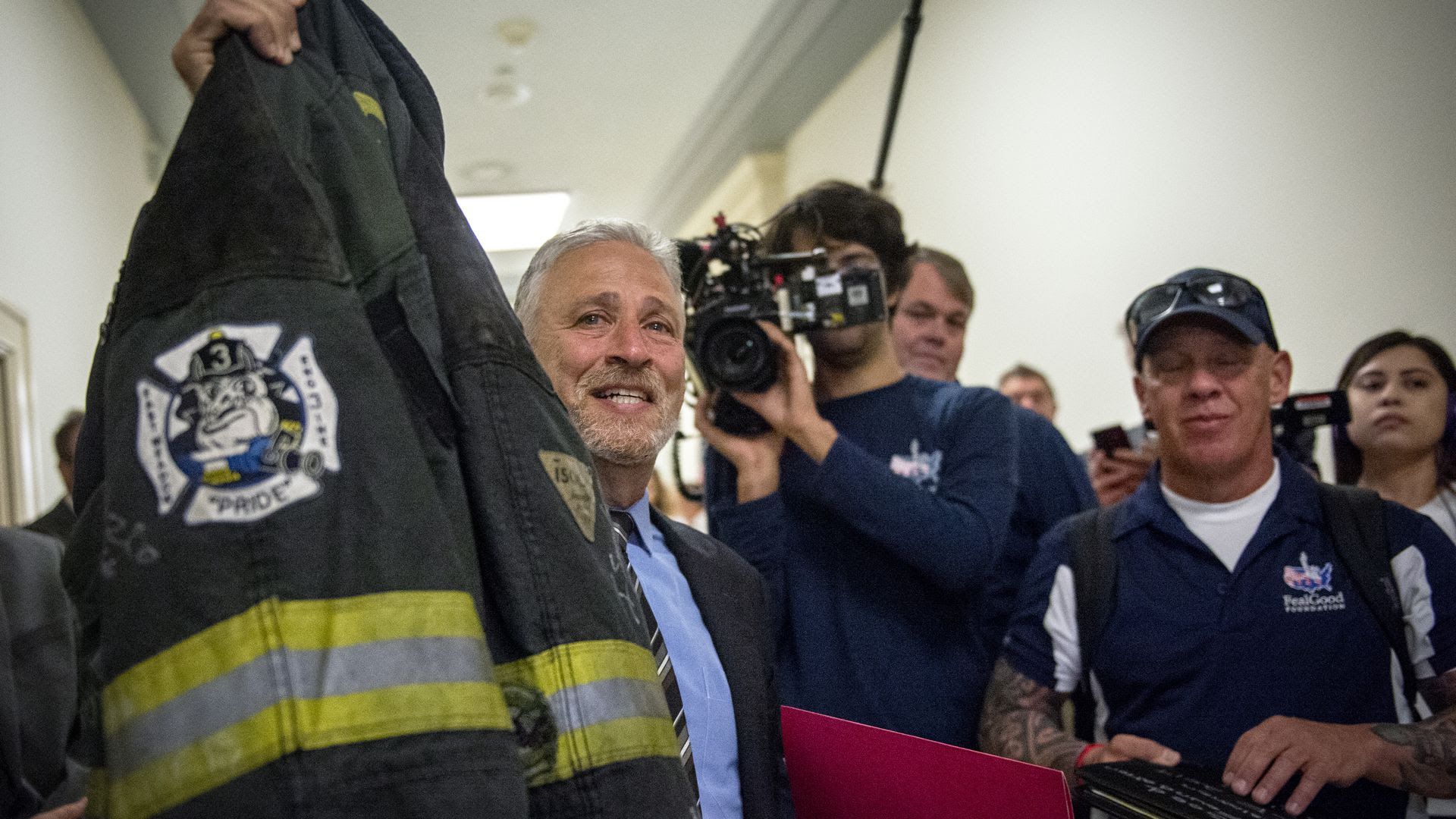 Jon Stewart holds up the jacket of first responder Ray Pfeifer before testifying at a hearing before the House Judiciary Committee in June. 
