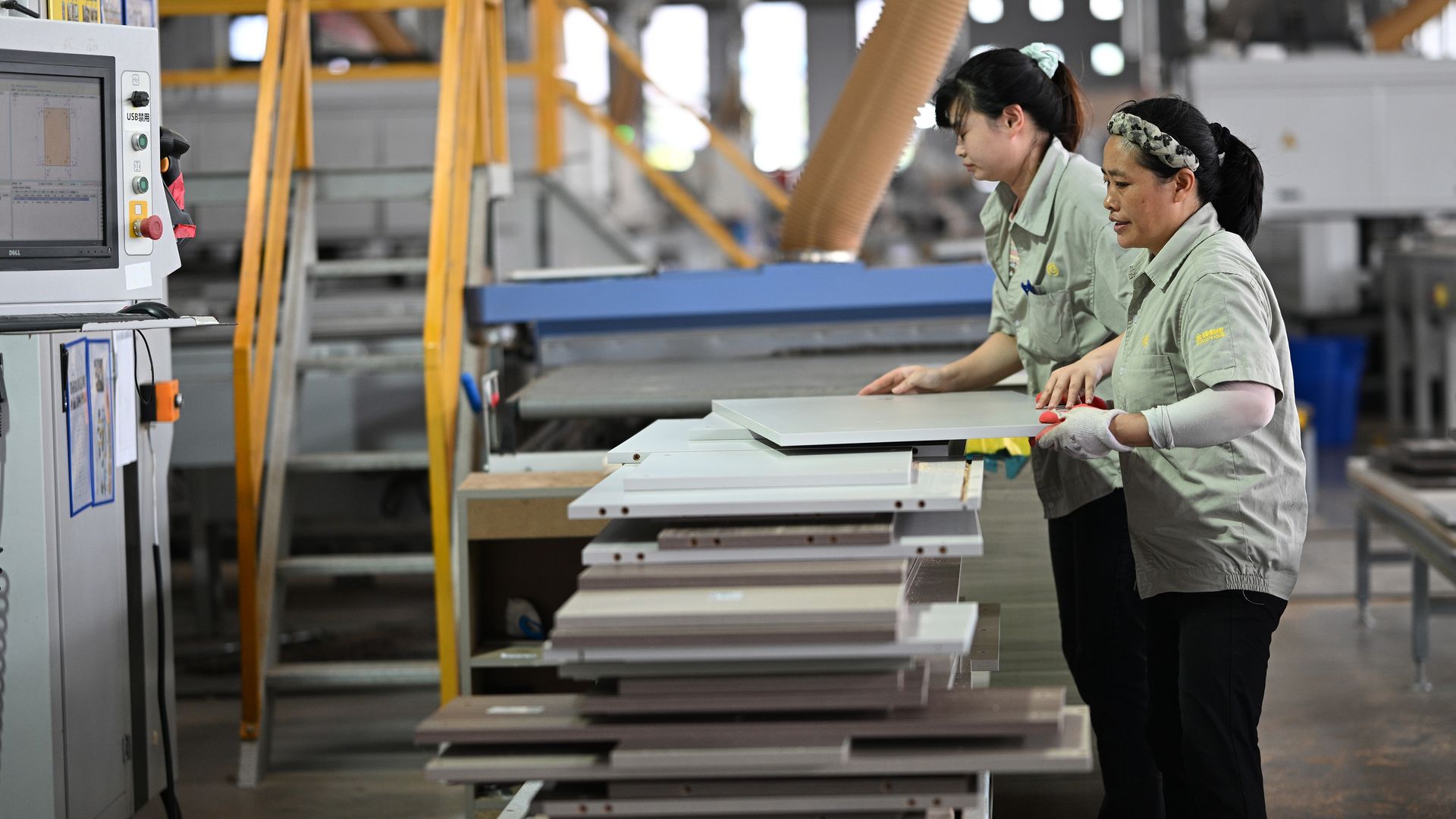 Workers in a factory assemble components of a kitchen cabinet. 