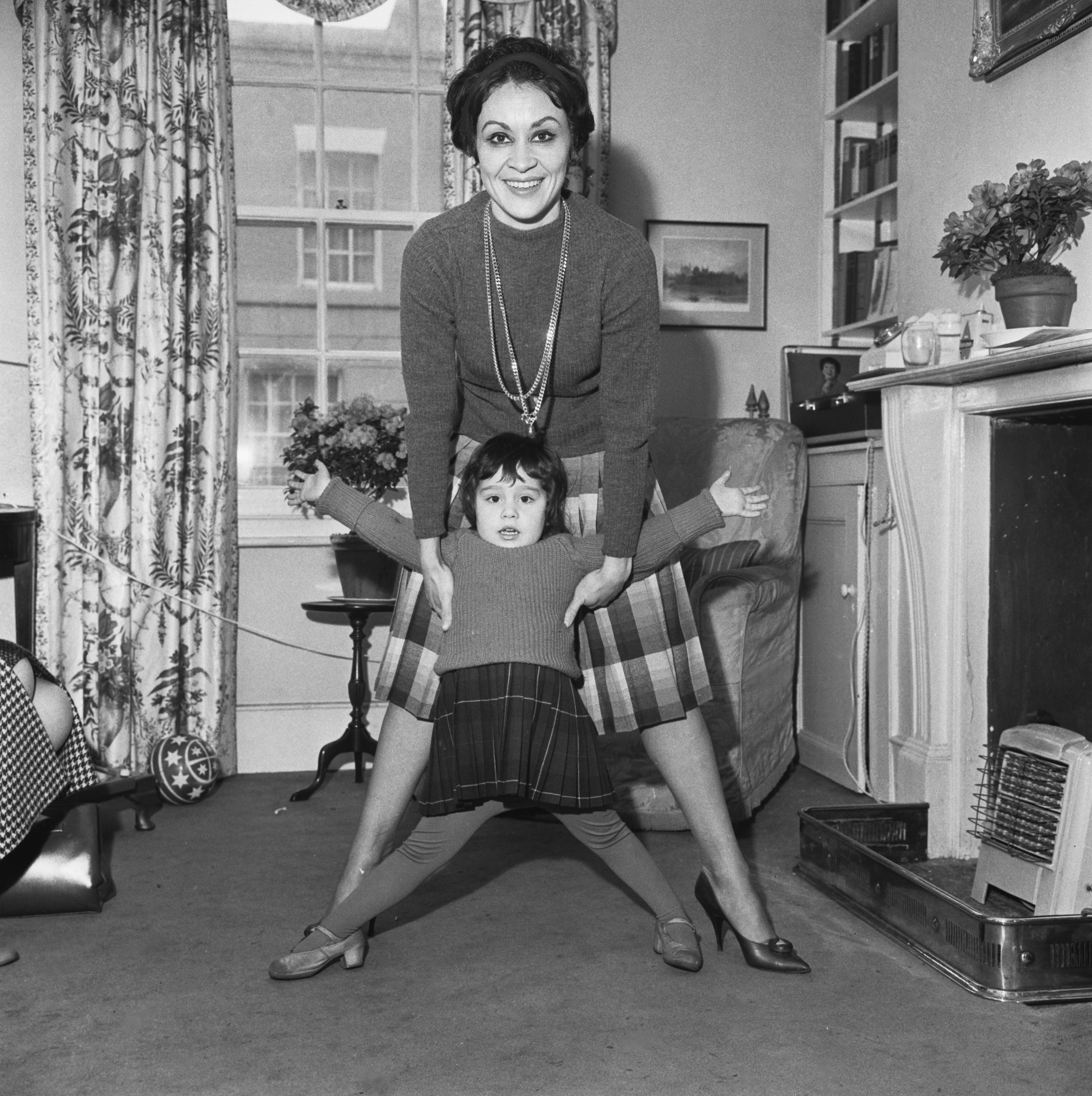 Chita Rivera bends over while holding up her young daughter, both posing for a photo inLondon