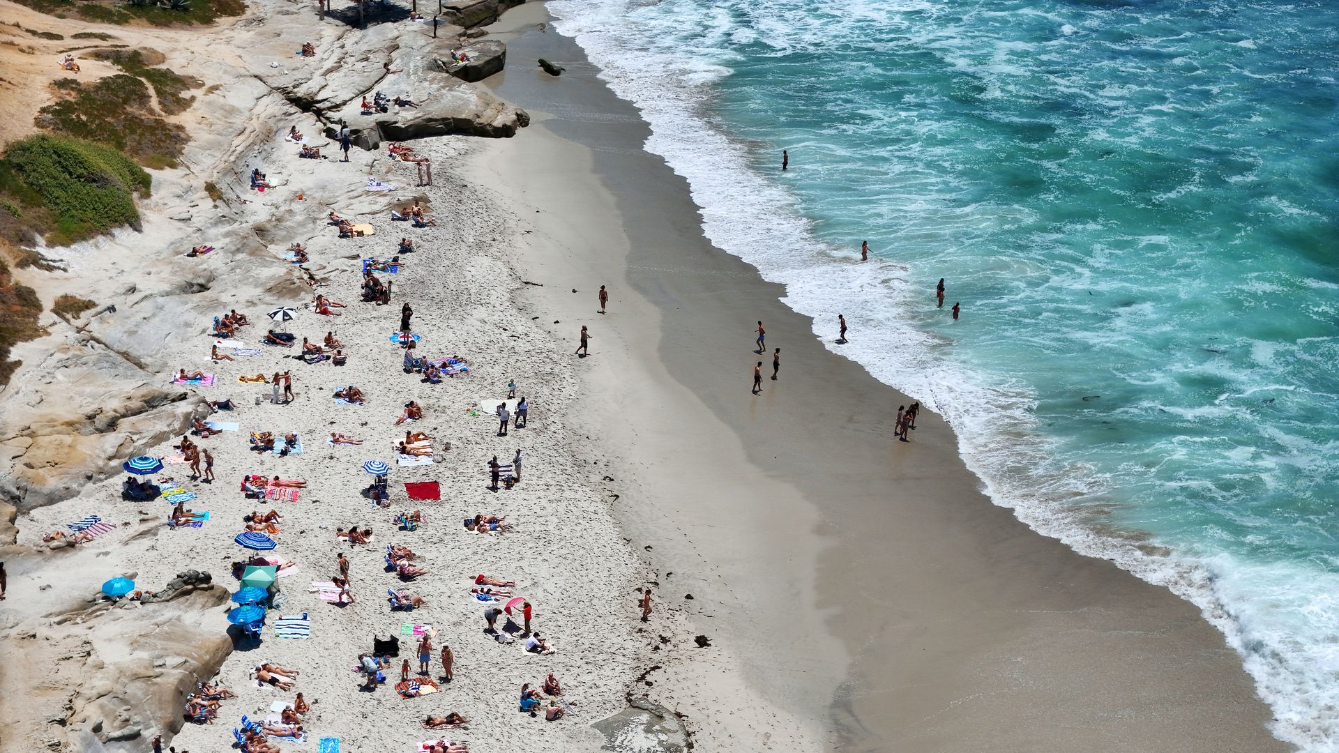 In an aerial view, people sunbath on the beach as waves break along the coastline of Windansea Beach in La Jolla after the National Weather Service issued a beach hazard statement for elevated surf and high risk for rip currents on June 20, 2026 in San Diego, CA.