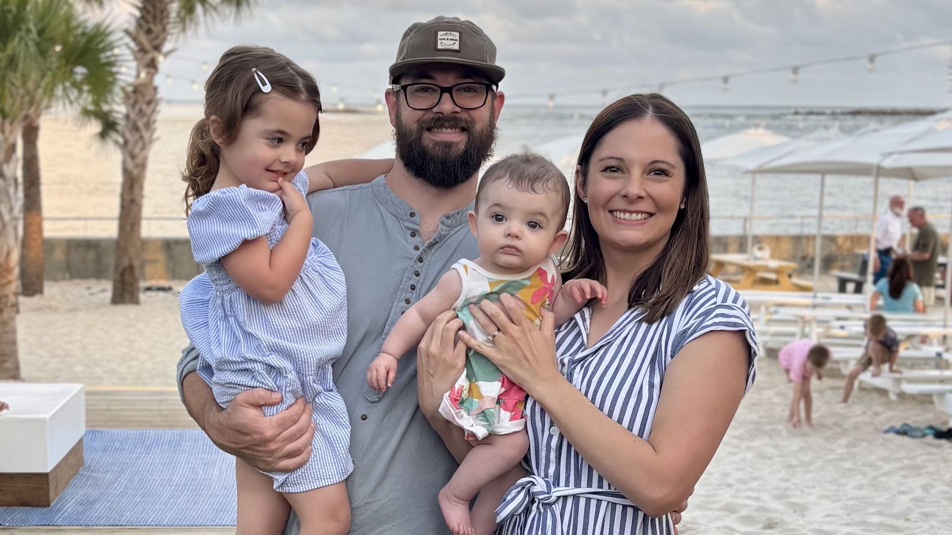 A photo of a family at the beach showing two adults holding two young girls