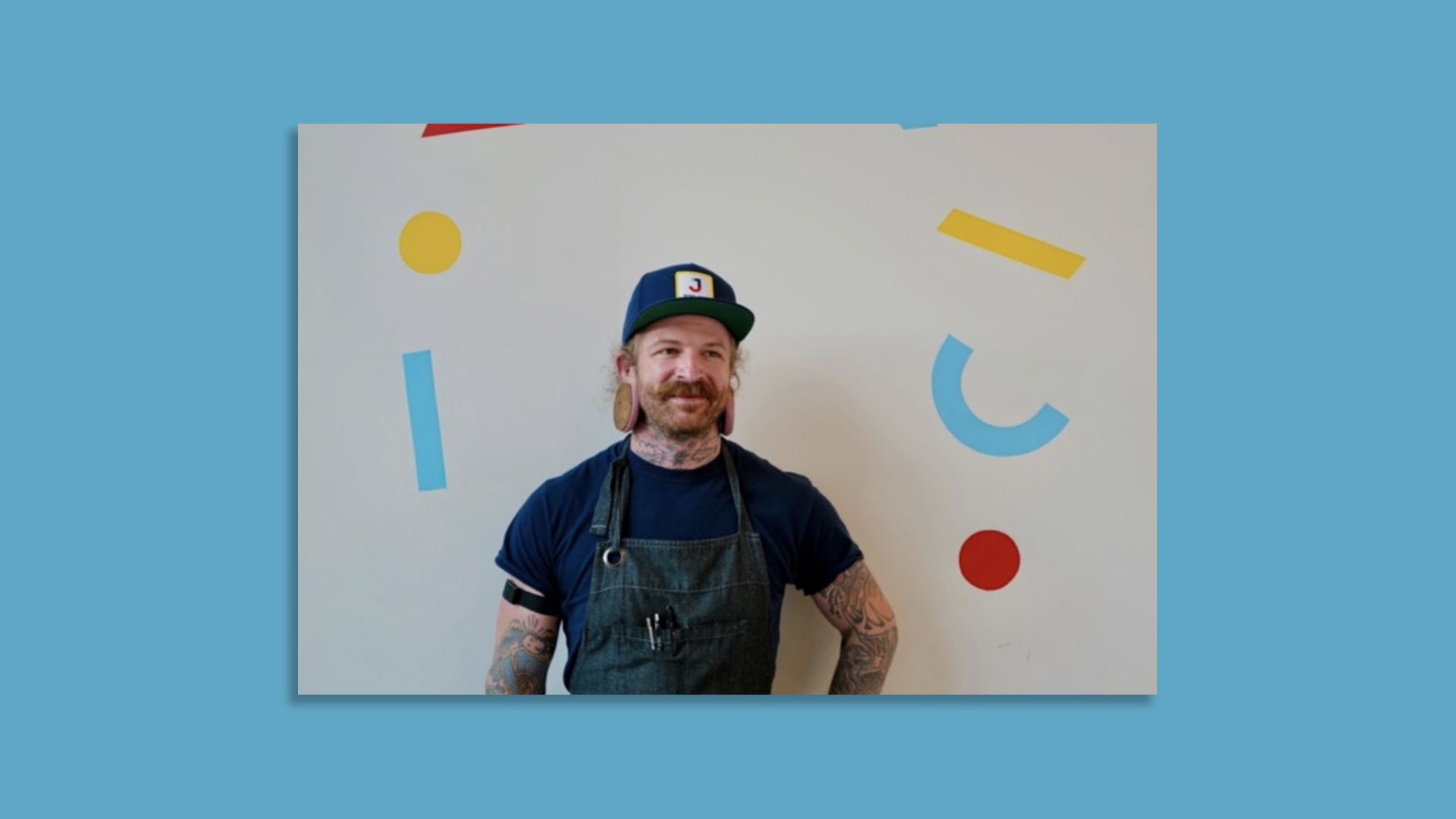 Man posing for a portrait in a chef's apron against a background of brightly colored swirls and dots.