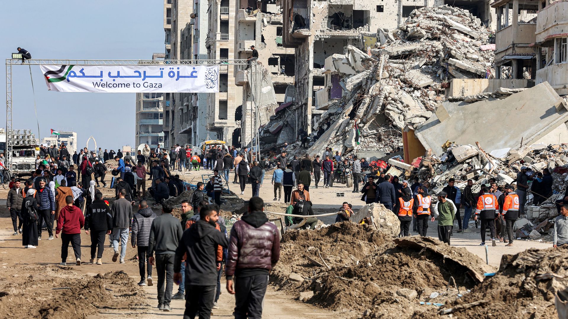  People gather by a banner welcoming people near the rubble of a collapsed building along Gaza's coastal al-Rashid Street for people to cross from the Israeli-blocked Netzarim corridor from the southern Gaza Strip into Gaza City on January 26, 2025. 
