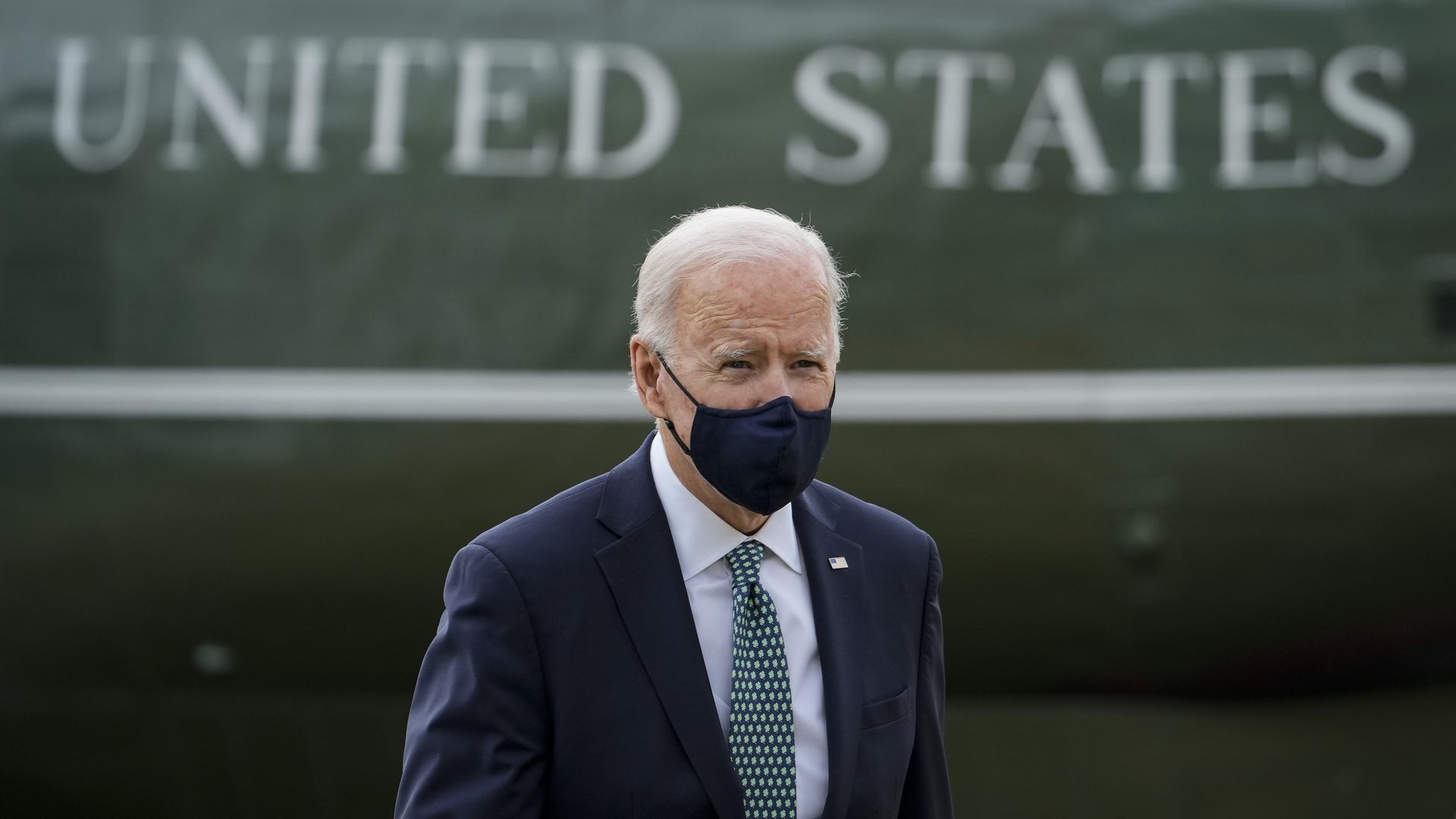 President Biden is seen walking in front of the words 