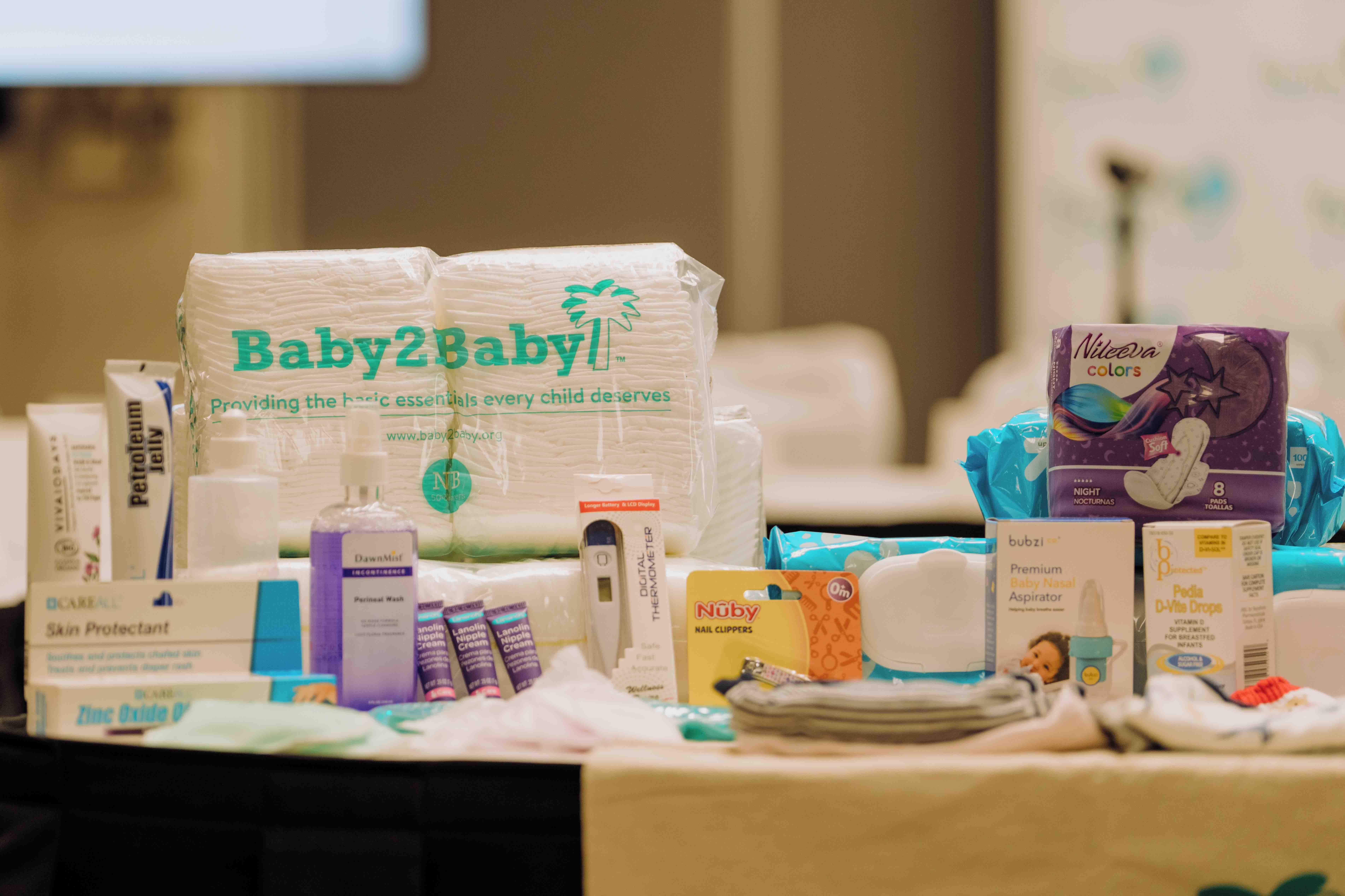 Photo shows newborn supplies like diapers and a baby thermometer that are included in the Baby 2 Baby care kit