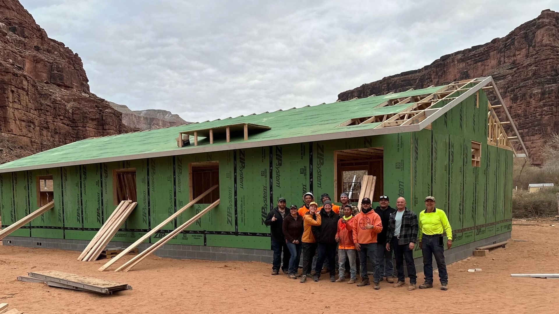 A group of people posing outside of a house that's under construction in a desert canyon.