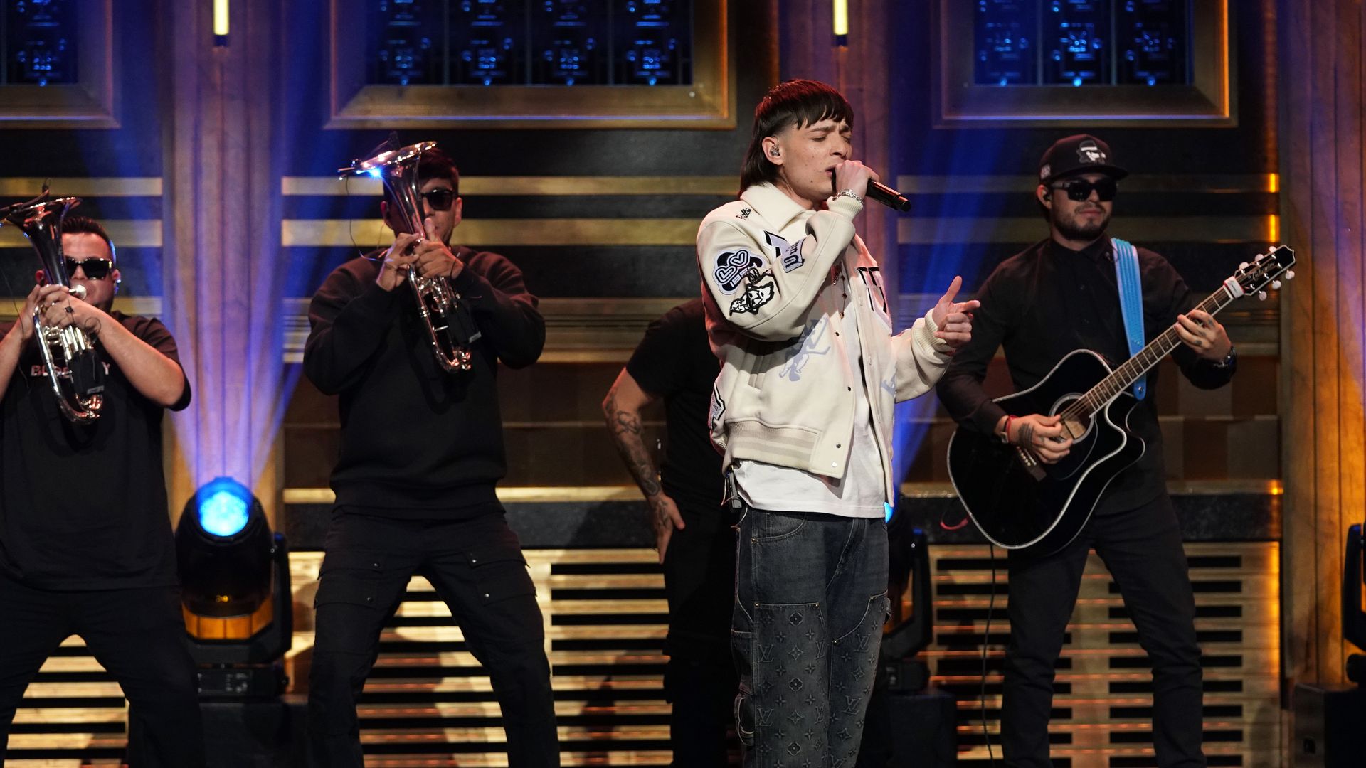 Peso Pluma sings on stage with his eyes closed and a band behind him.