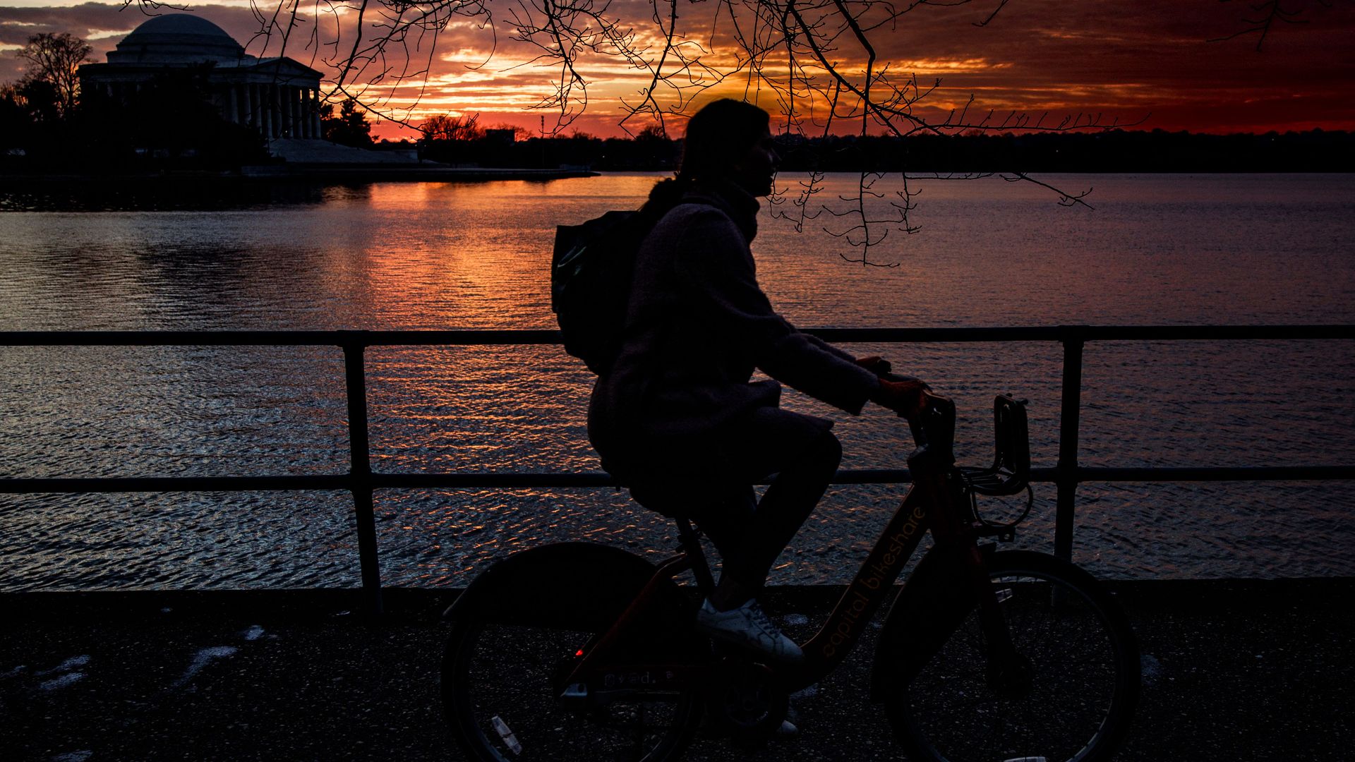 The silhouette of a person riding a bike in front of the Thomas Jefferson memorial at sunset.