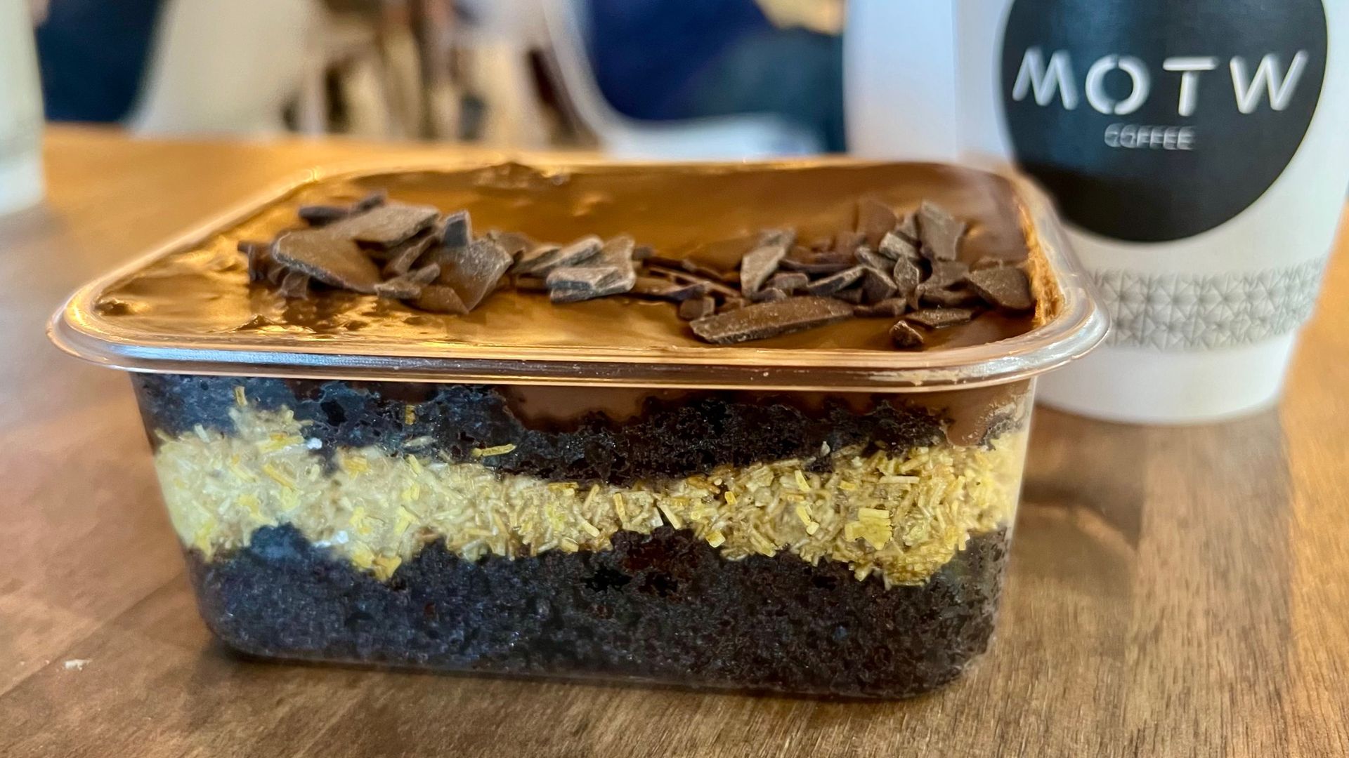 A clear rectangular container with two layers of brownie with a crunchy green filling