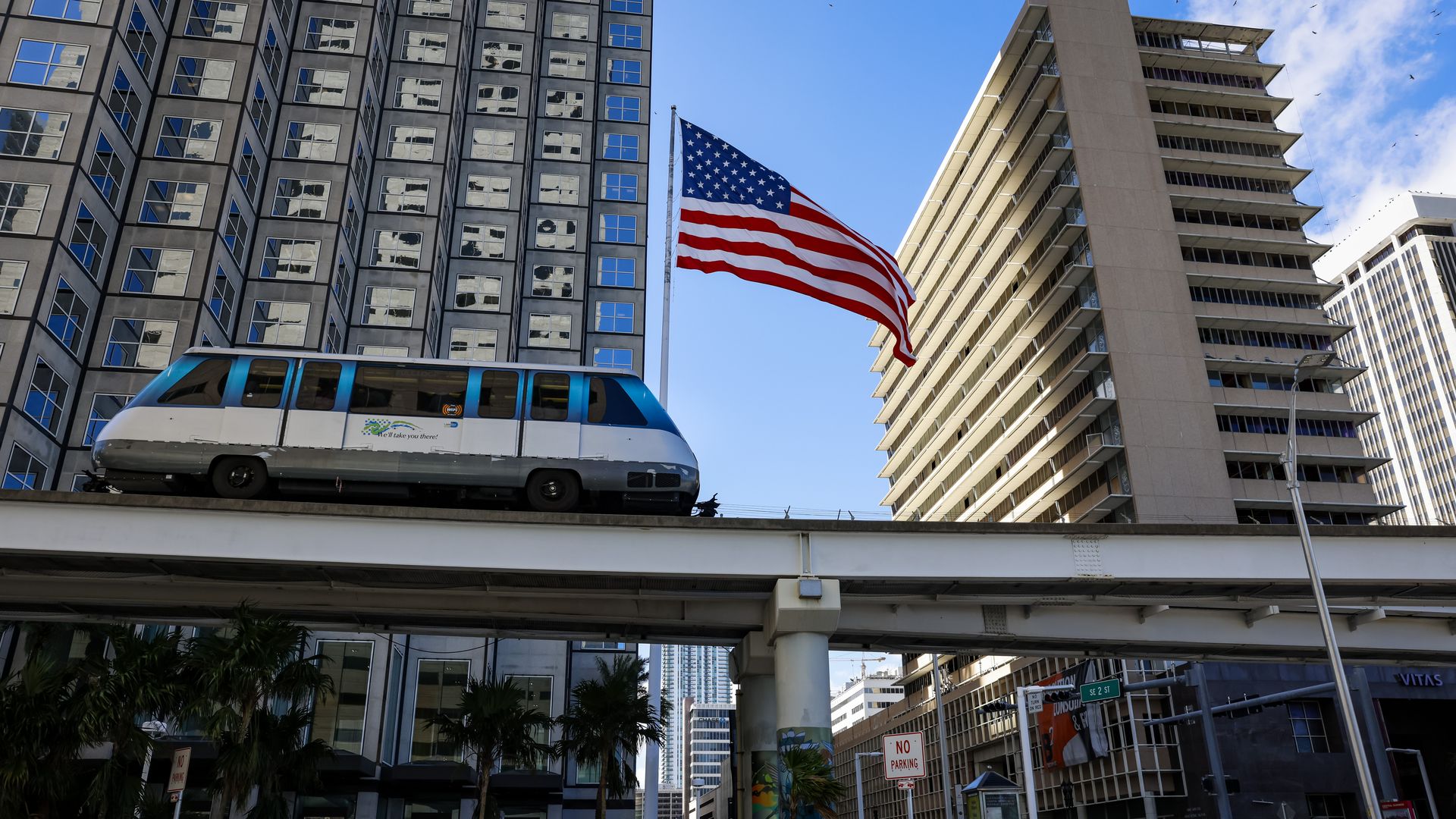 Miami's Metromover rail system in front of buildings downtown and an American Flag.