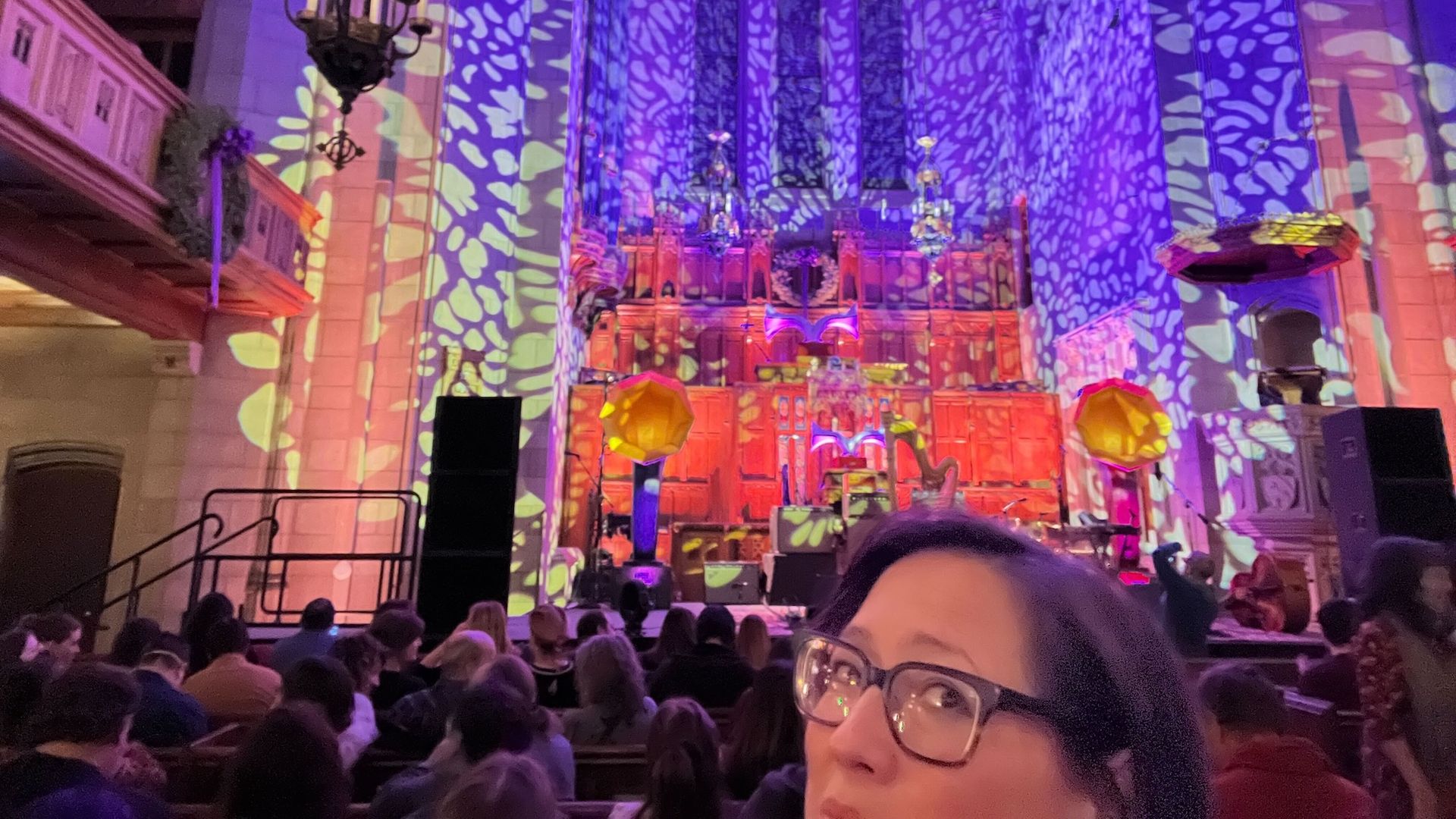 Neon bright colors projected on a the back of a stage with the top of a woman's head.