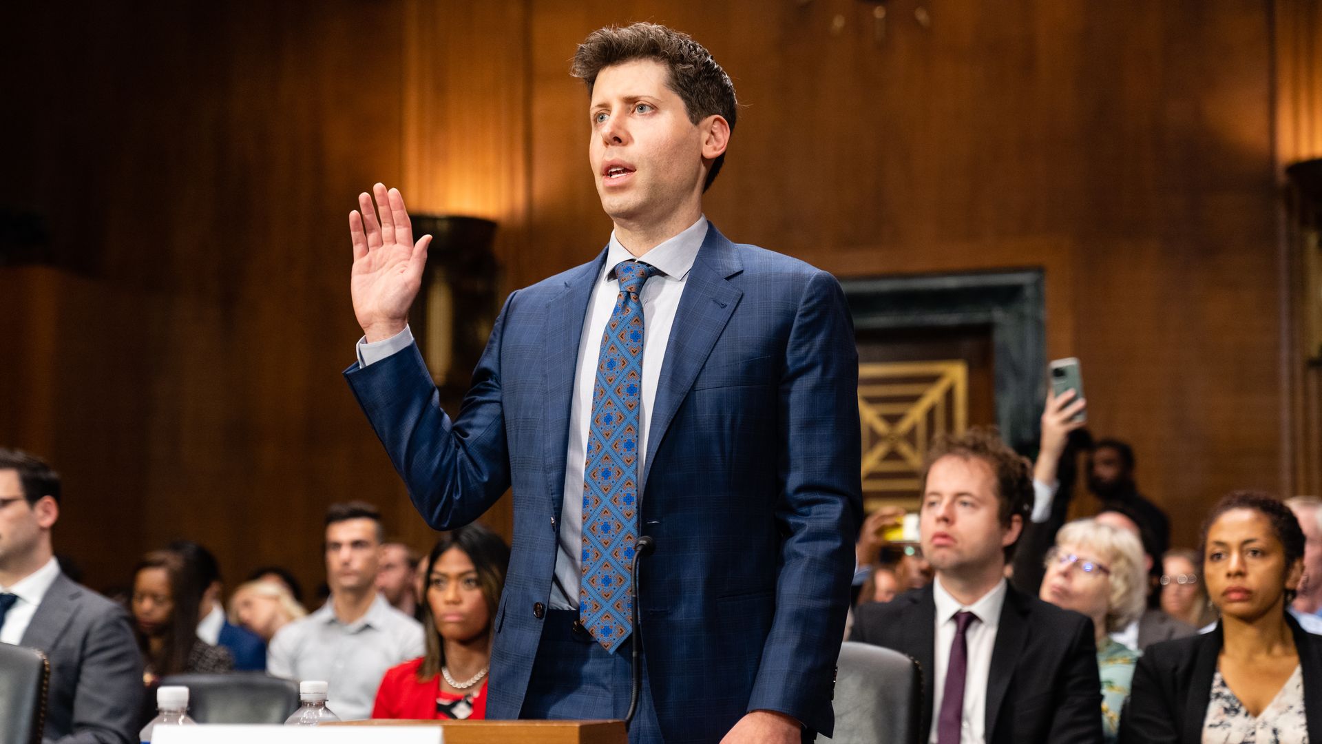 OpenAI CEO raises his hand to swear to tell the truth in a Senate room wearing a blue suit