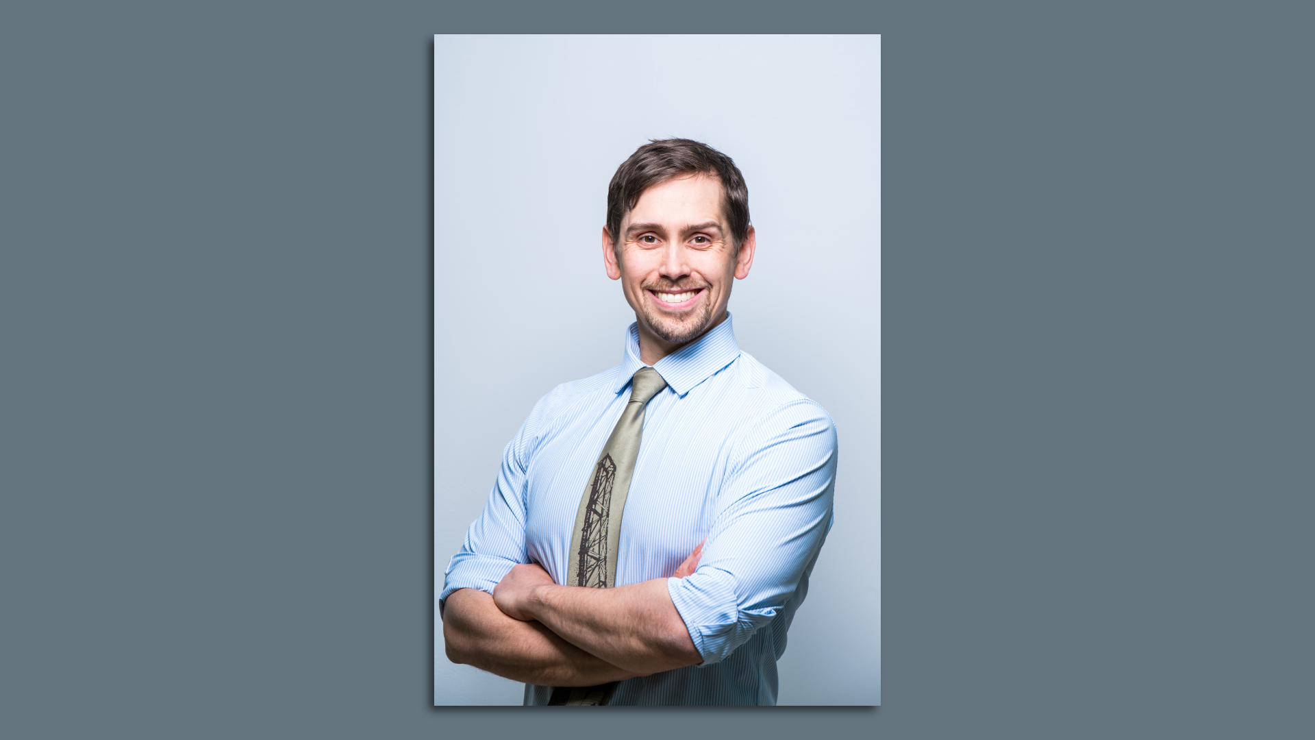 Headshot of white man with brown hair in blue shirt and gold tie. Rolled up sleeves.