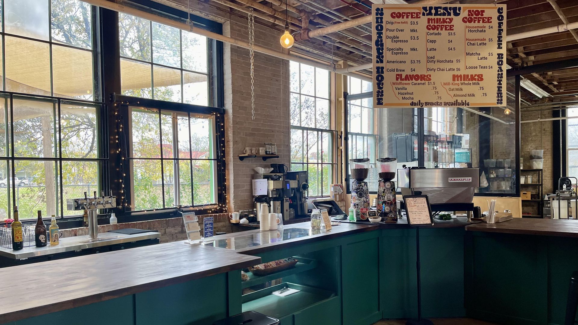 A green coffee bar with a wood top and a hanging menu sign from the ceiling.