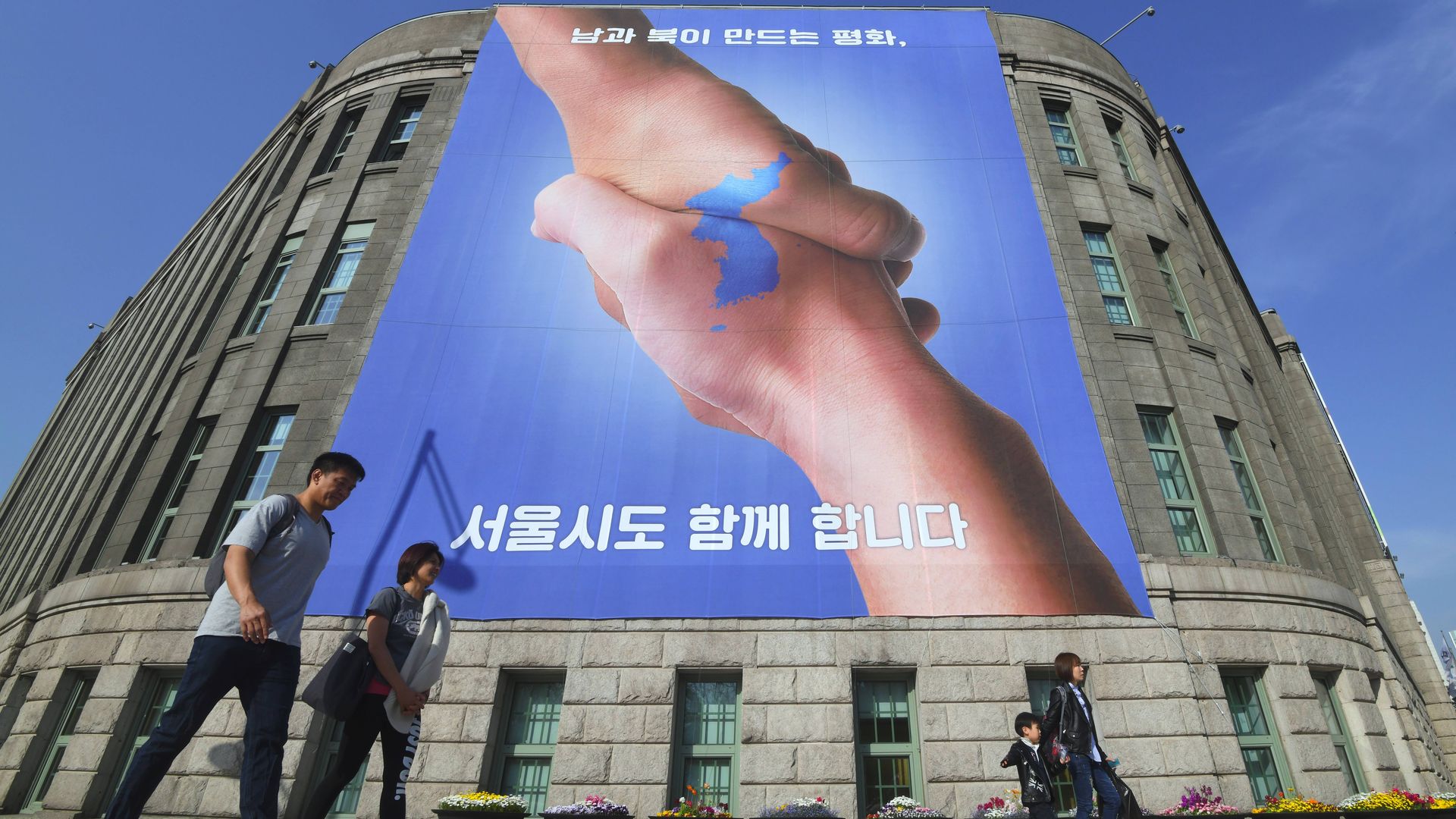 Pedestrians walk past a banner showing two hands shaking to form the shape of the Korean Peninsula to support the upcoming inter-Korean summit