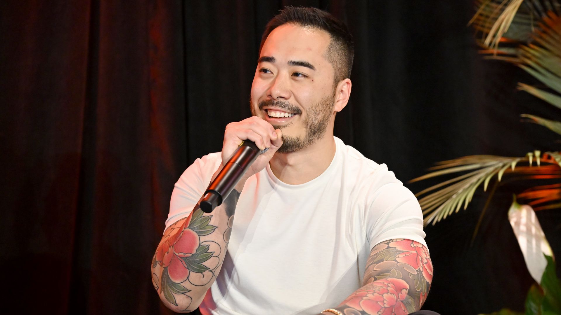 Jesse Ito smiles while holding a microphone on a stage. 