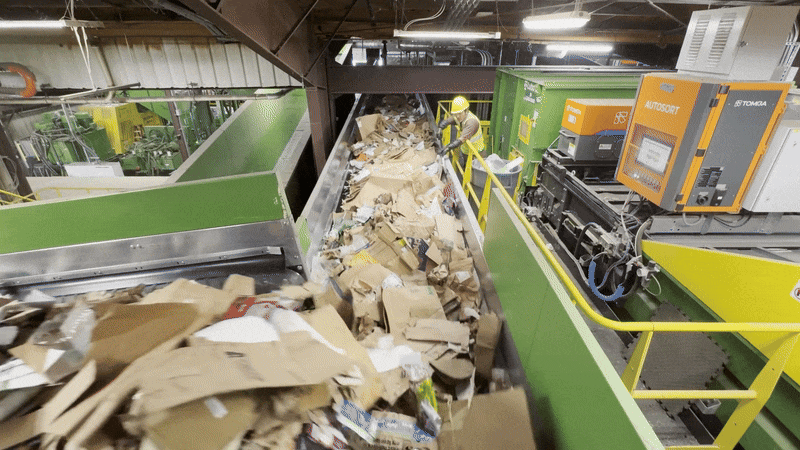 Animated gif shows conveyor belts moving large amounts of cardboard through a recycling facility.