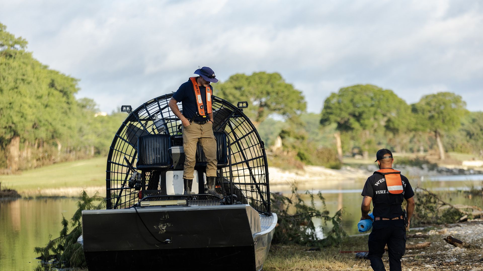 A rescue worker stands on a water boat while another rescue worker stands nearby