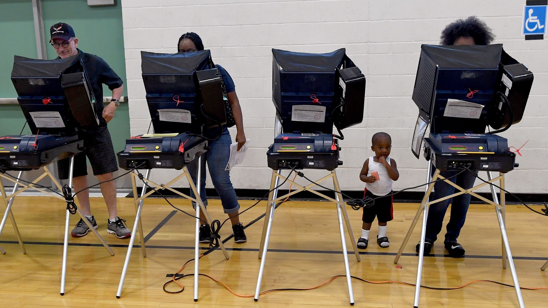 Voters cast their ballots at voting machines in school gym.