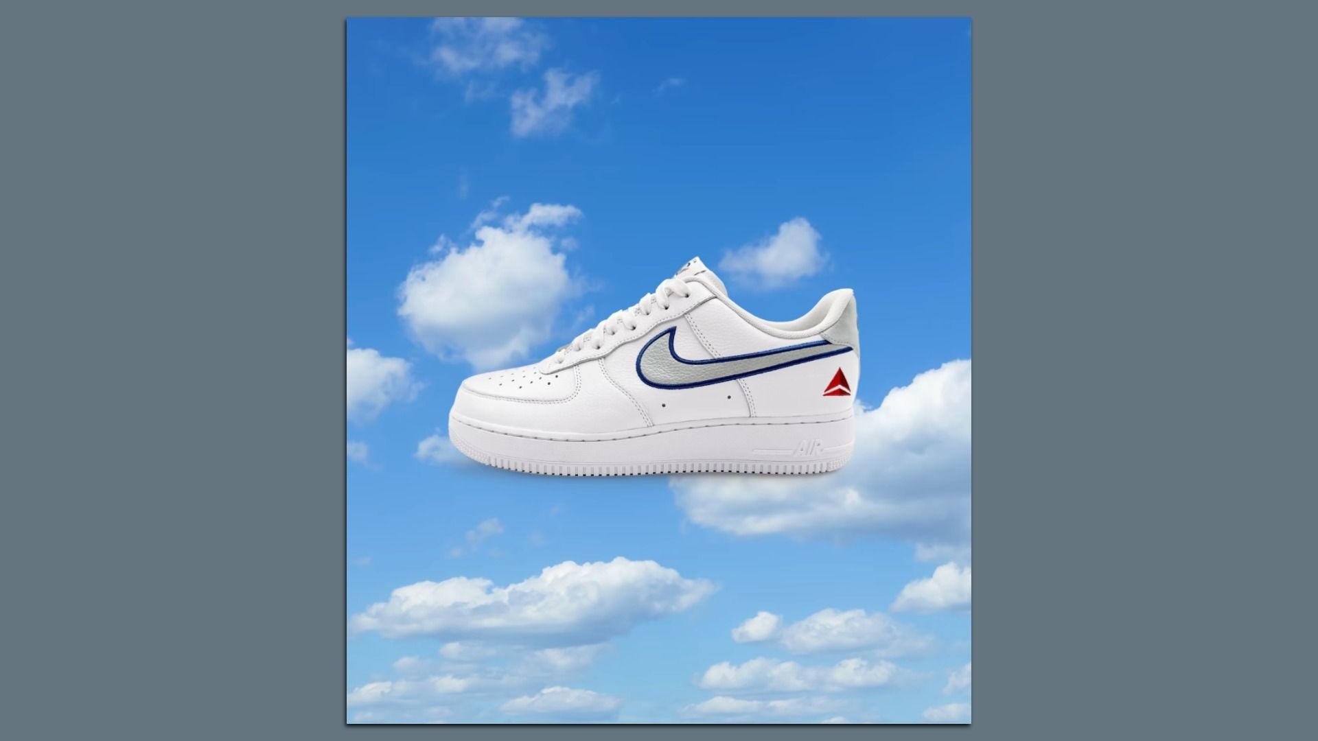 White sneaker with navy blue swoosh outline and red triangle logo on heel, floating against a bright blue sky with scattered white clouds.