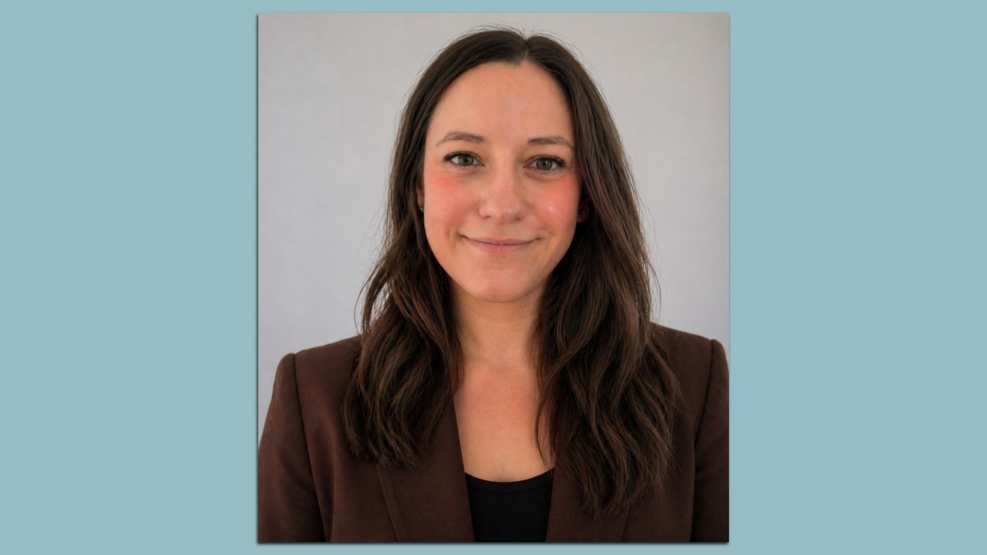 Smiling portrait of a woman with long brown hair, wearing a brown blazer over a black top, against a light gray backdrop; the image is framed by a blue-gray page.