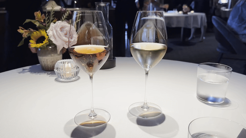 A video of two glasses of sparkling wine bubbling gently as they sit on a white tablecloth-covered table.