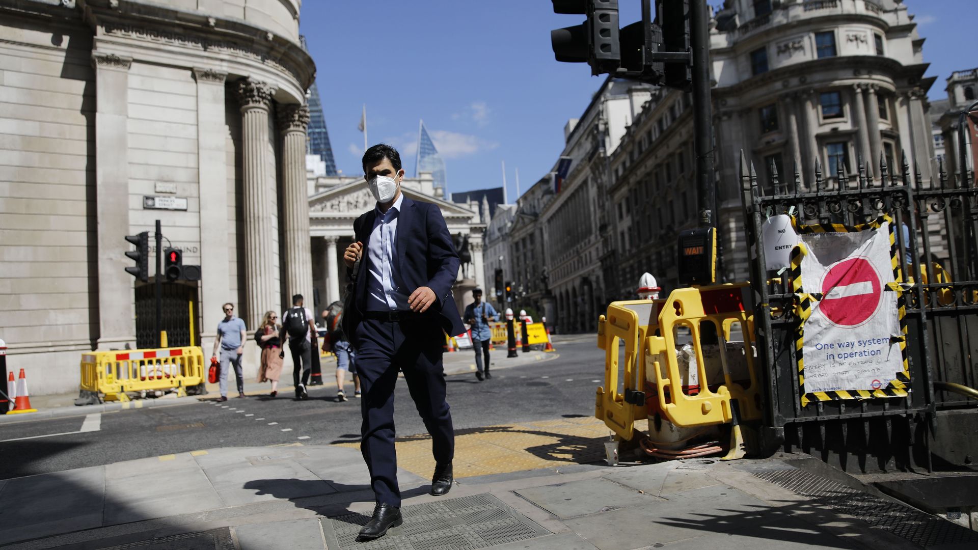 A man wearing a face mask walks near the Royal Exchange and the Bank of England in the City of London on July 17