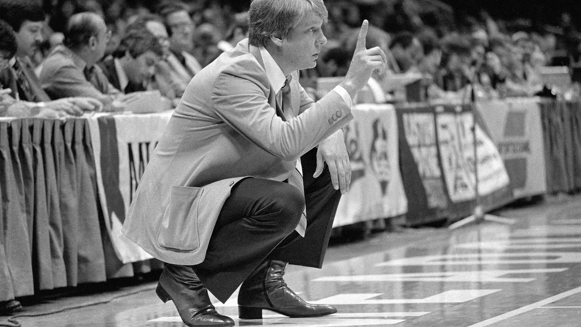 In a black-and-white photo, Don Nelson, head coach of the Golden State Warriors, squats and looks on and calls a play during a game against the Boston Celtics at the Boston Garden circa 1990.