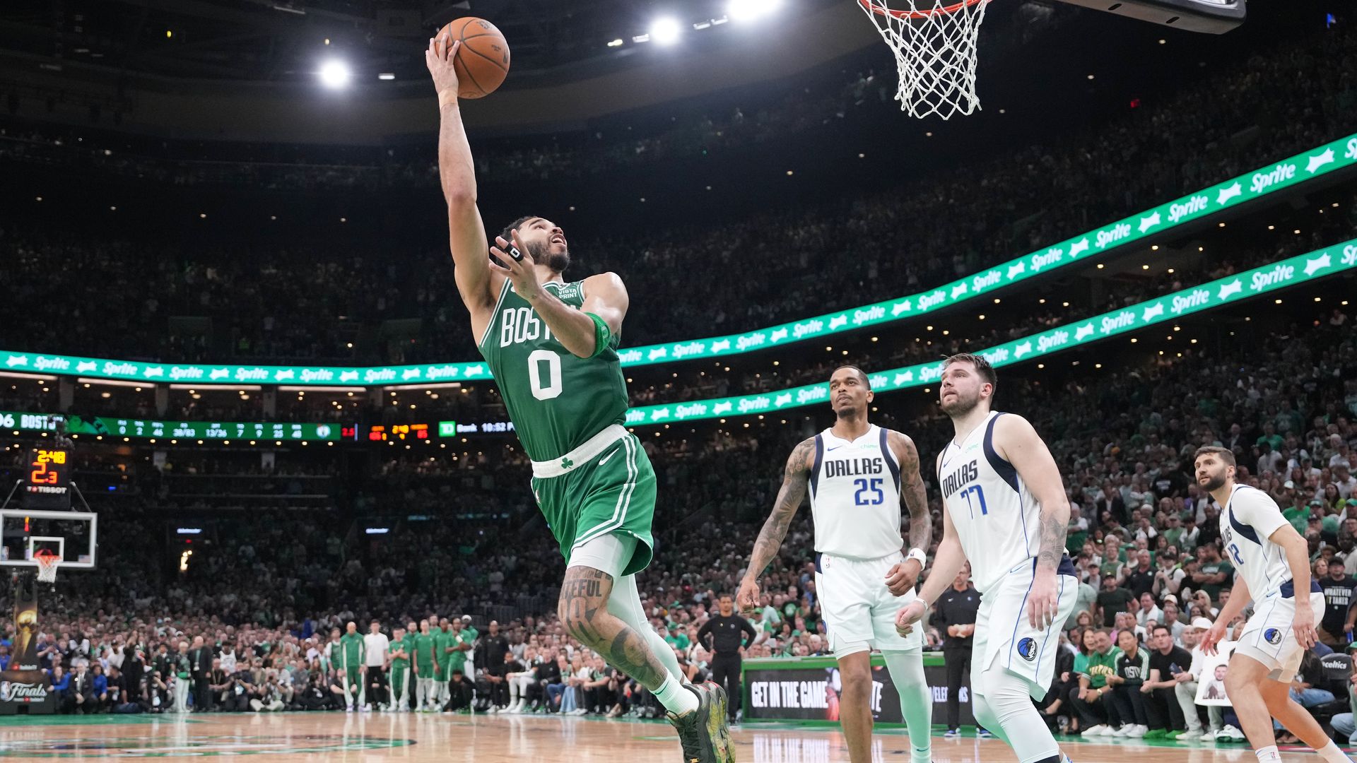 A basketball player leaps in the air with three other players from the other team watching him