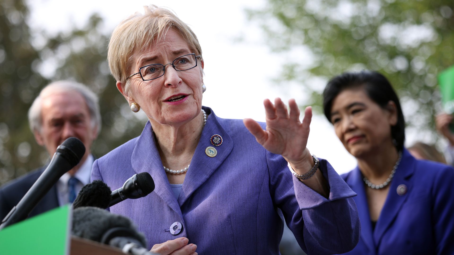 Rep. Marcy Kaptur, wearing a purple pantsuit and speaking at a podium with a green sign.