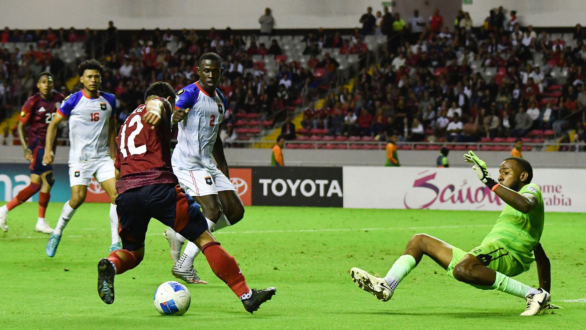 Costa Rica's forward #12 Randy Vega tries to dribble past Belize's goalkeeper during a game.