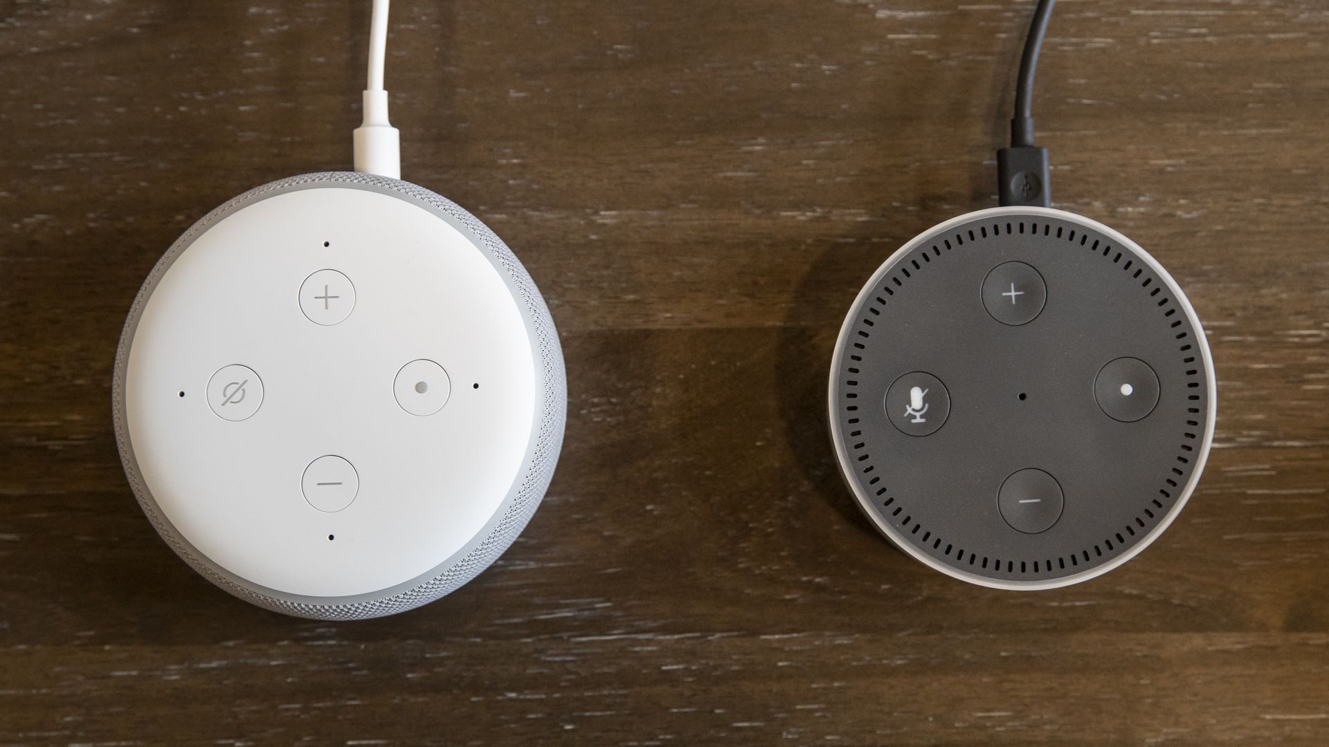 This image shows two Amazon echo dots sitting side by side on a wooden table.