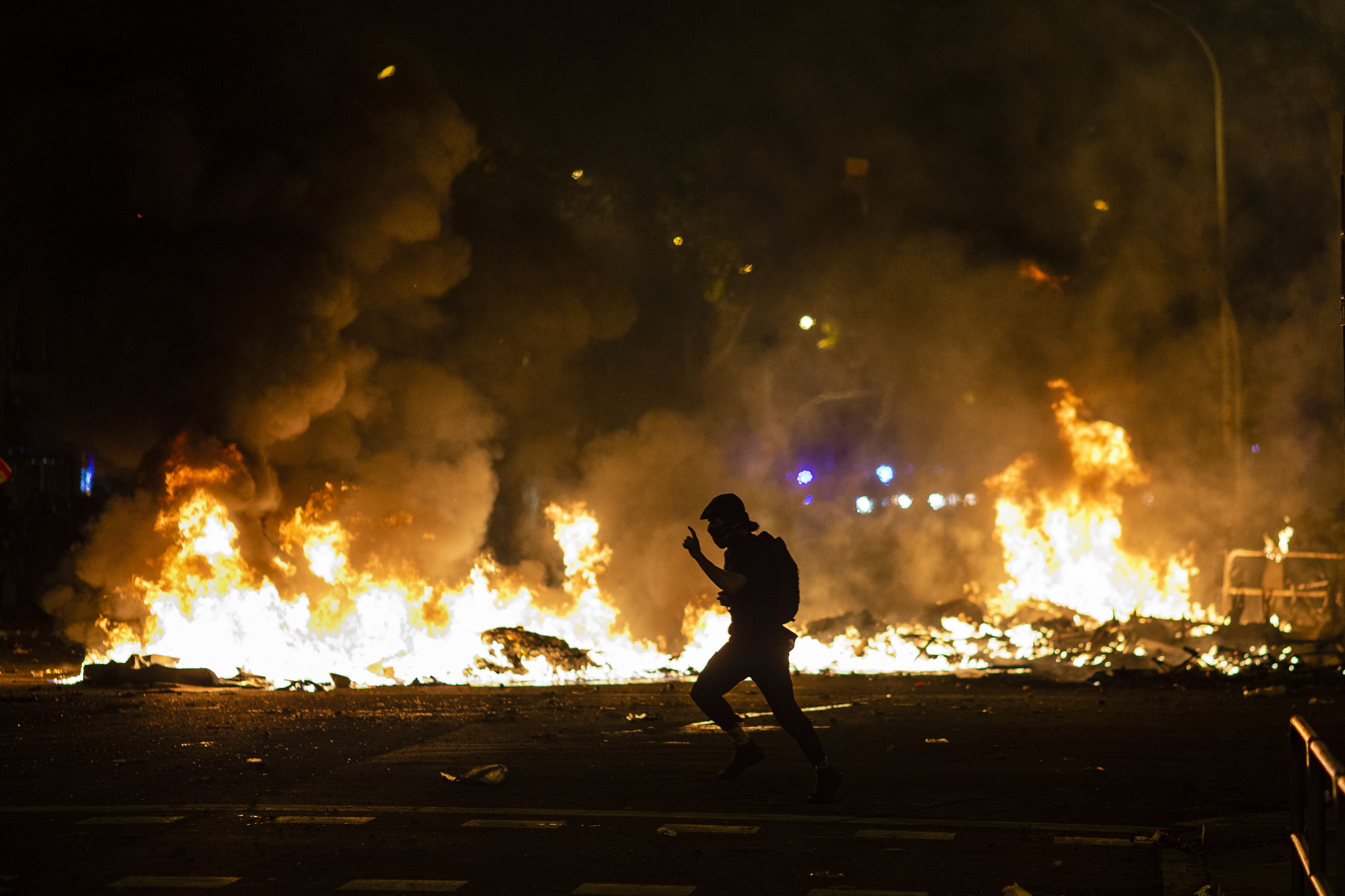 In this image, one person walks next to a line of fire in the street at night