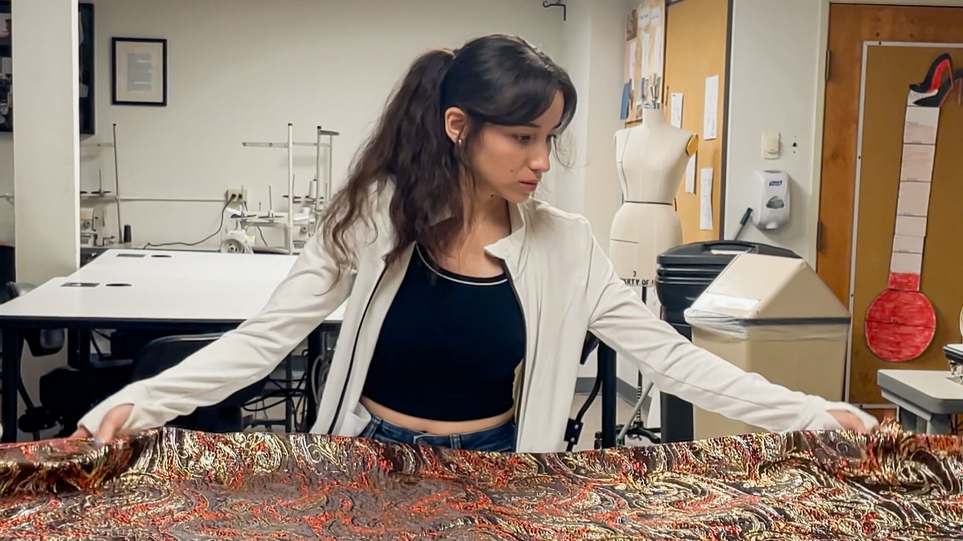 A young woman measures patterned material in a sewing room. 