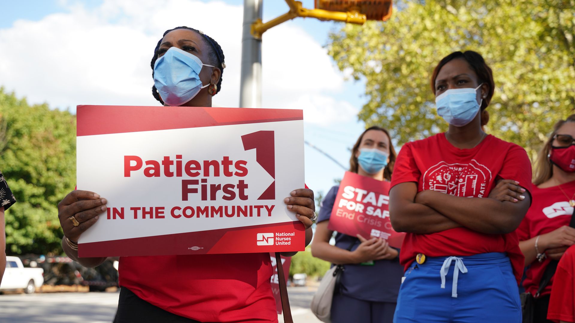 Photo of a masked person holding a sign that says "Patients First" at a rally protesting staffing shortages