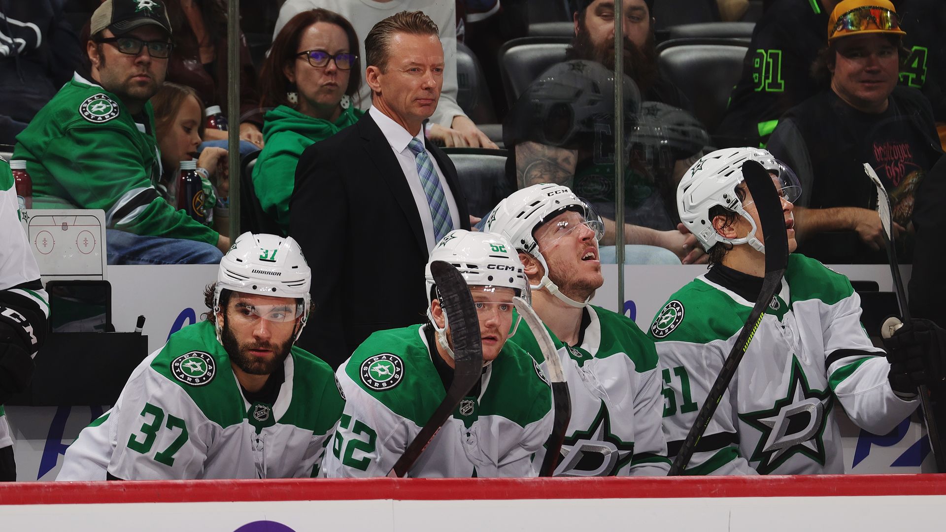 A man wearing a suit stands behind four hockey players 