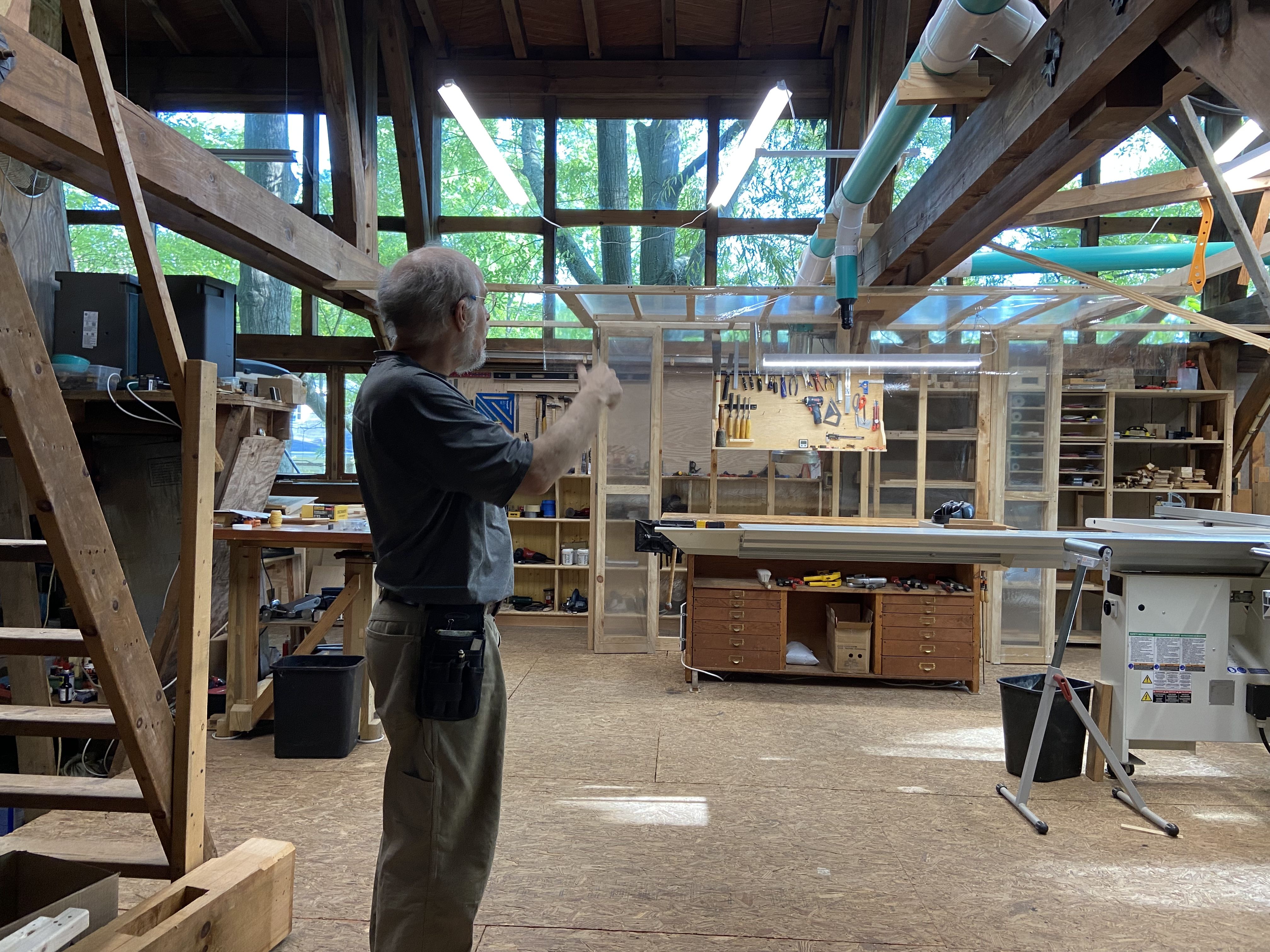 A man gestures toward his workshop in a large light-filled room with medieval ceilings 
