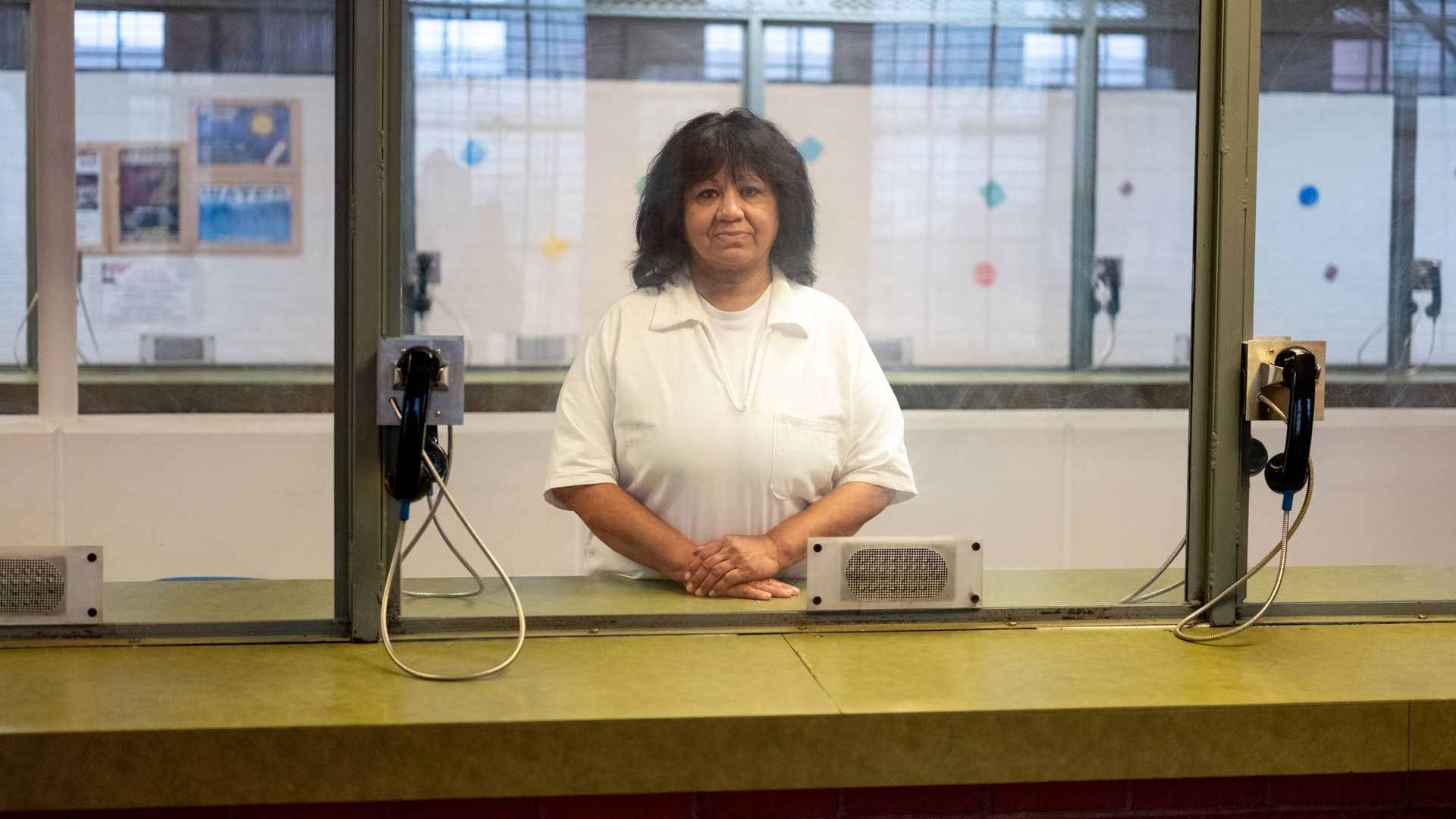 Melissa Lucio stands behind a glass wall in a prison in Texas while wearing a white jumpsuit