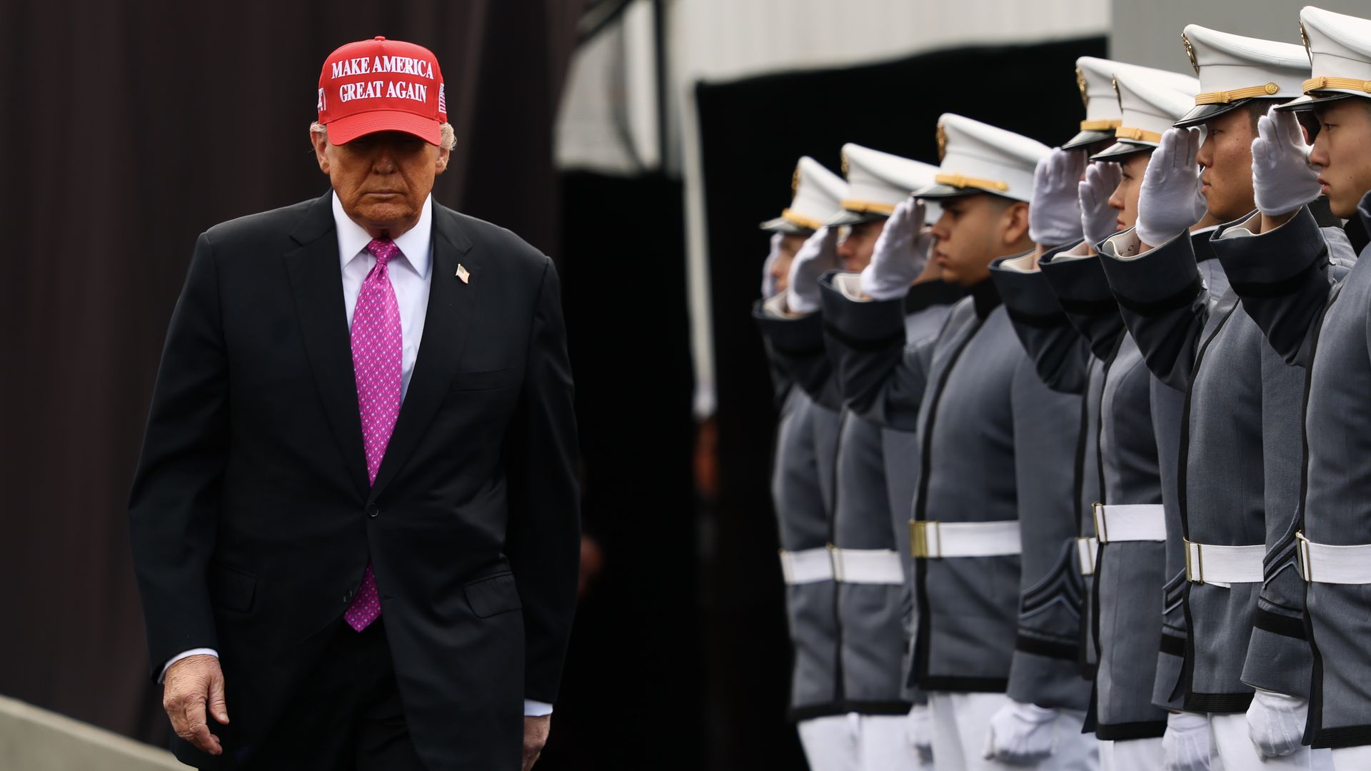 President Trump in MAKE AMERICA GREAT AGAIN red hat with line of men saluting him