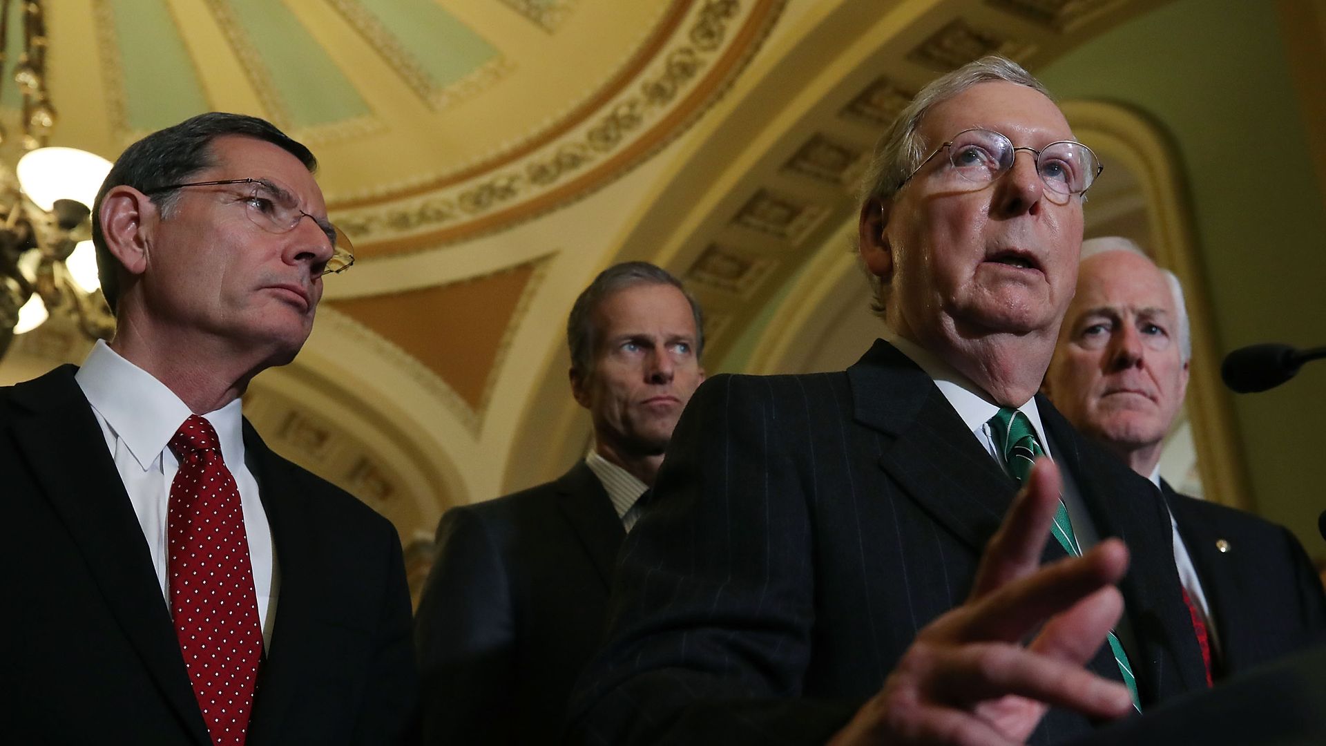 Four people wearing suits and ties under a domed ceiling