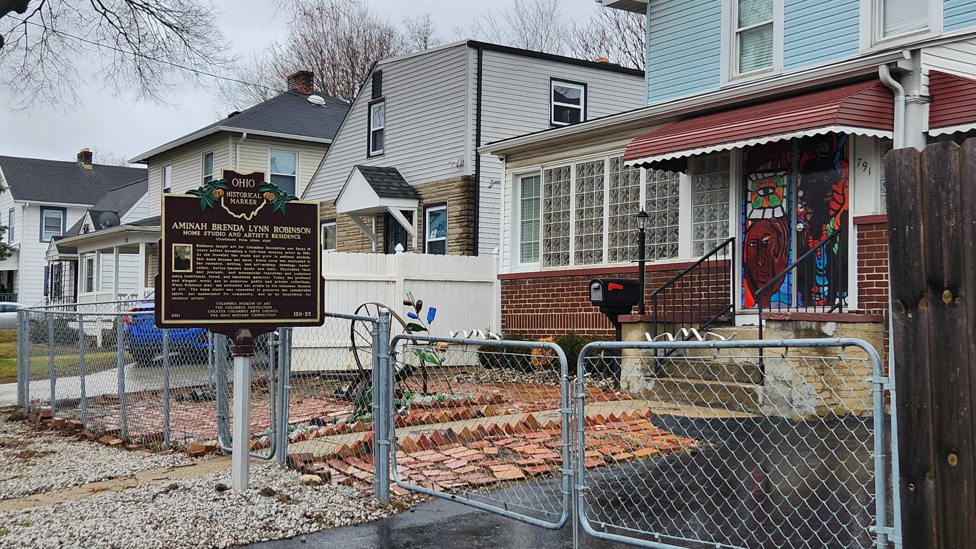 A historical marker for Aminah Brenda Lynn Robinson outside her home, with colorfully-painted doors. 