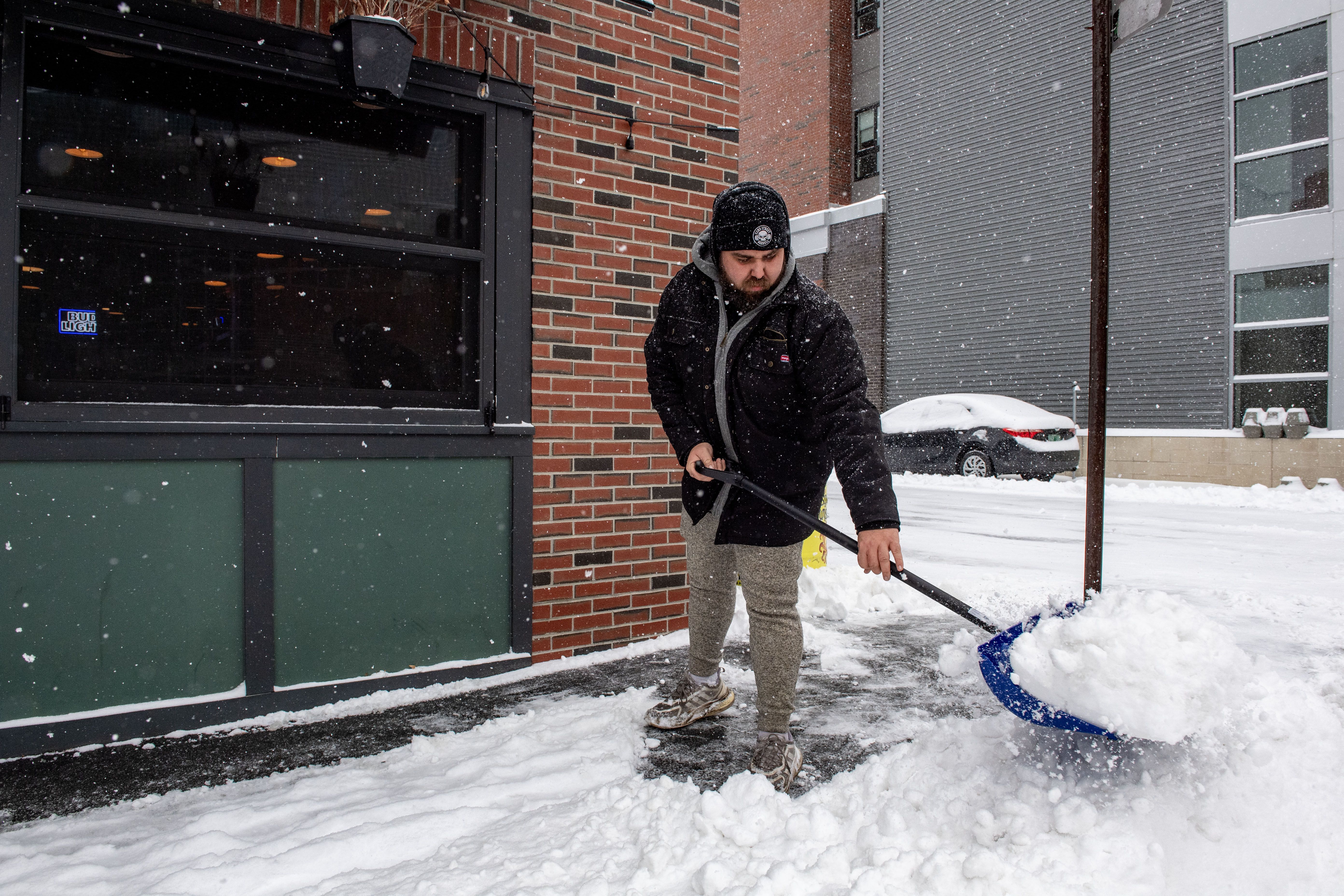 A person clears snow in front of a business in Manchester, New Hampshire on January 7, 2024. Forecasters warned on January 5 that a deluge of snow and wintery conditions could bring travel chaos to the US northeast this weekend, with some 25 million people subject to a storm warning. 