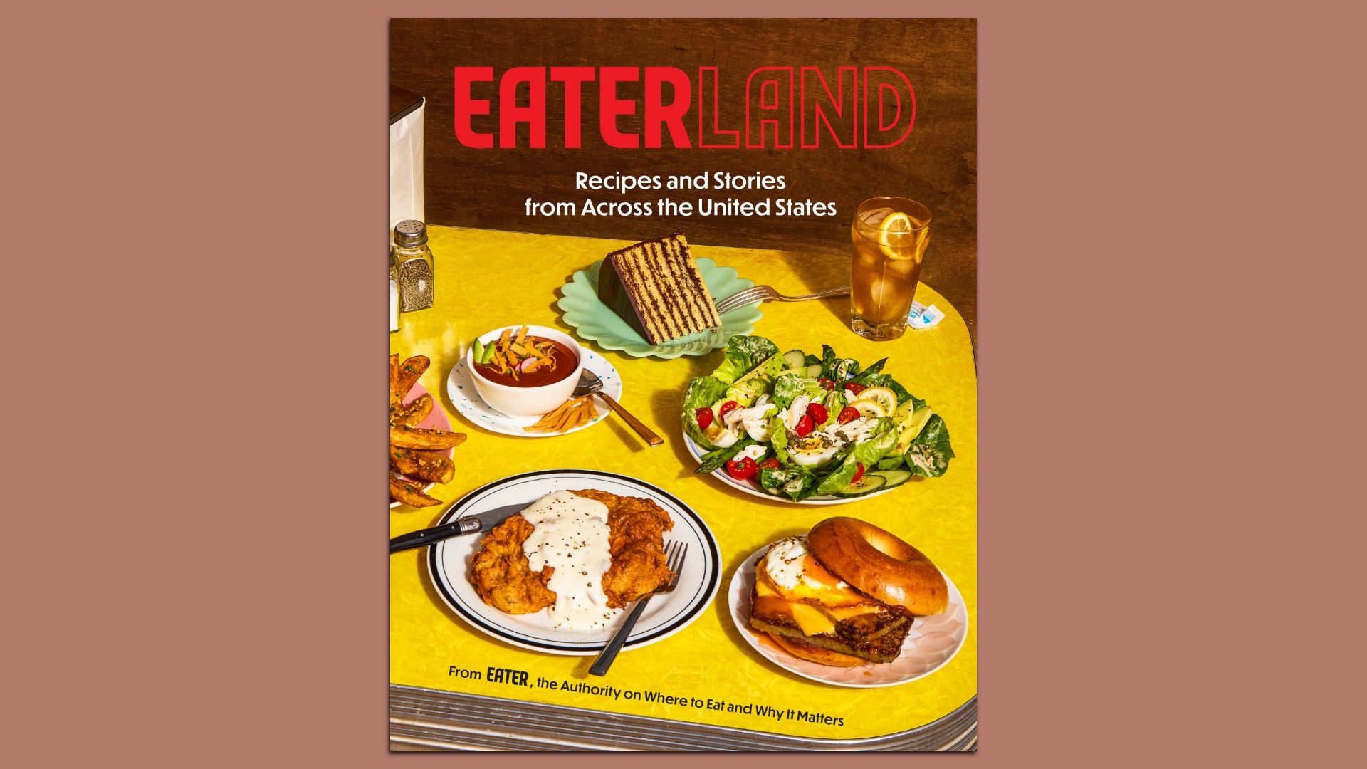 Cover image of a bright yellow table laden with food—salad, cake, fried chicken with gravy, a burger, and iced tea. Bold red title "EATERLAND" with subtitle "Recipes and Stories from Across the United States".