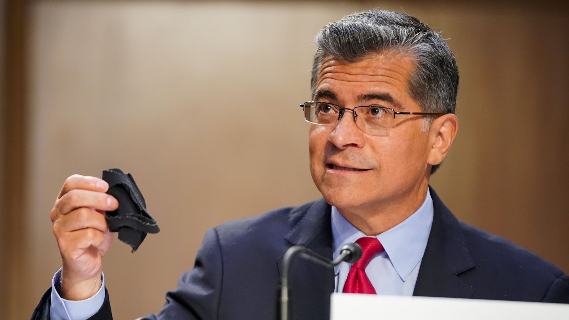 Secretary of Health and Human Services Xavier Becerra holds a mask up during a Senate Health, Education, Labor, and Pensions Committee hearing.