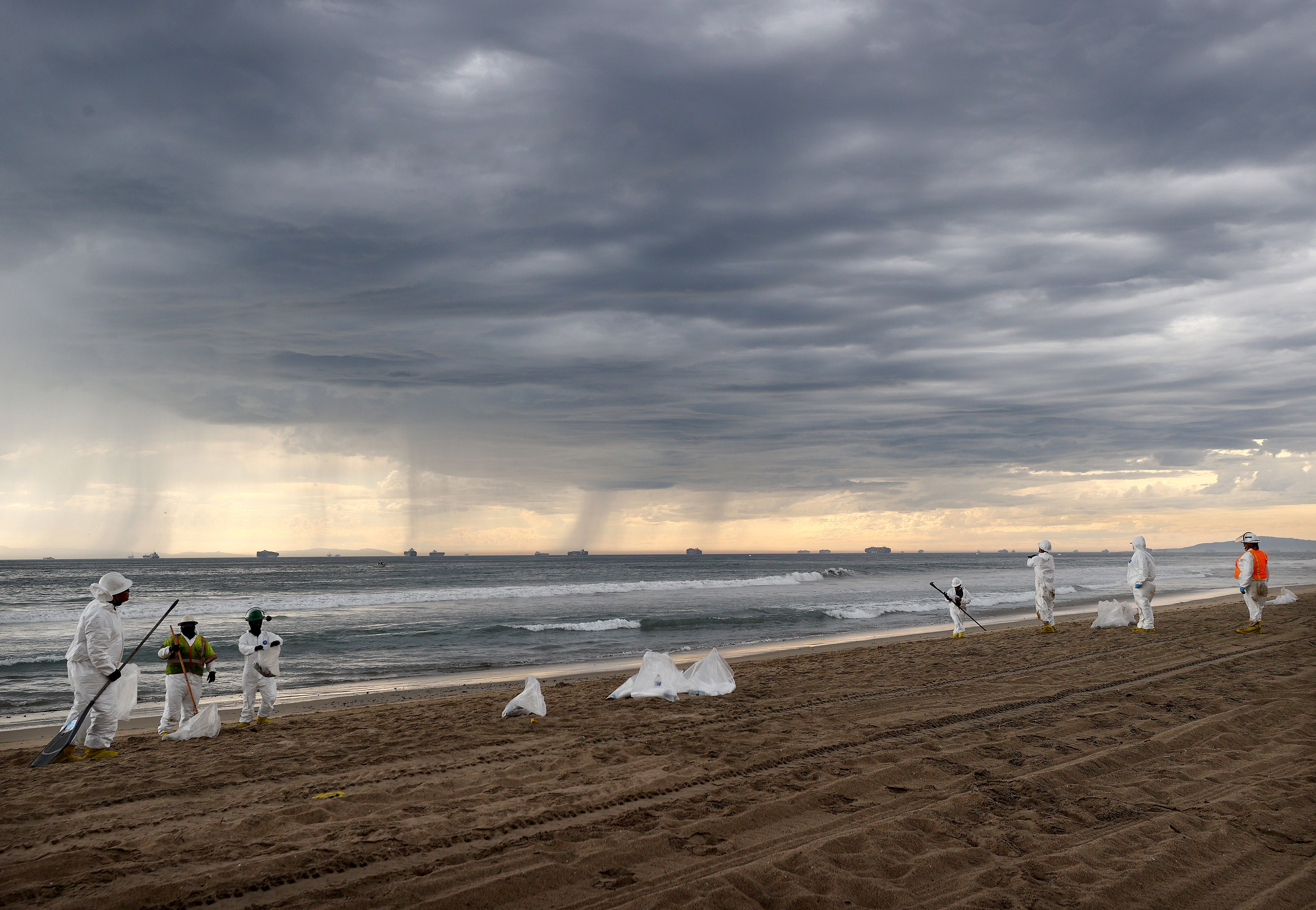 Cleanup workers in protective suits prepare to depart the closed Huntington State Beach as a storm approaches after a 126,000-gallon oil spill from an offshore oil platform on October 4