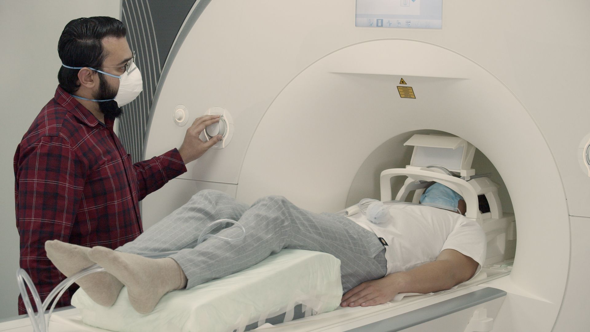 Image of a man in an MRI machine, while a scientist handles the controls