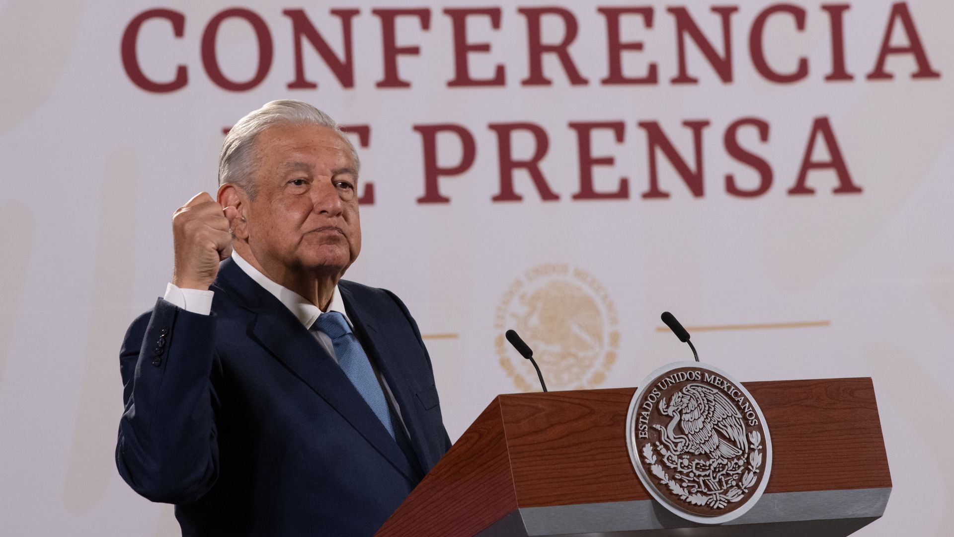The president of Mexico holds his fist up while standing in front of a podium at a news conference