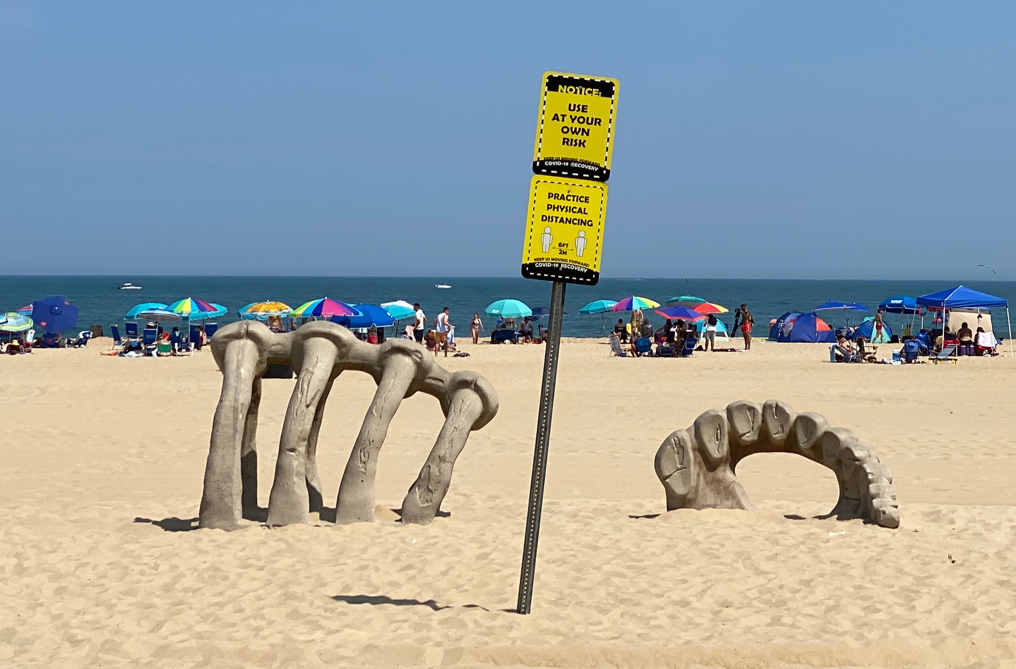 Tourist gather at the beach in Ocean City, Maryland as a sign says "Use at your own risk."