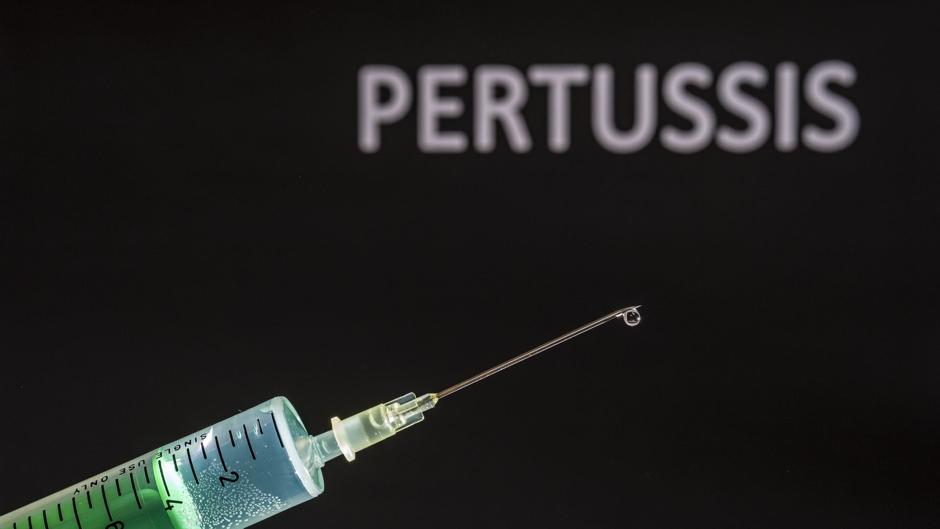 This photo illustration shows a disposable syringe with hypodermic needle, PERTUSSIS written on a black board behind.